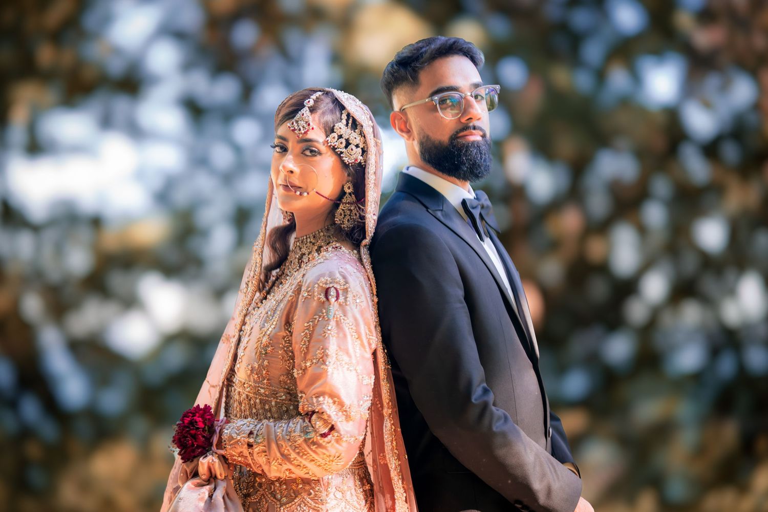 A couple in traditional South Asian wedding attire pose together during an outdoor photo session at sunset.
