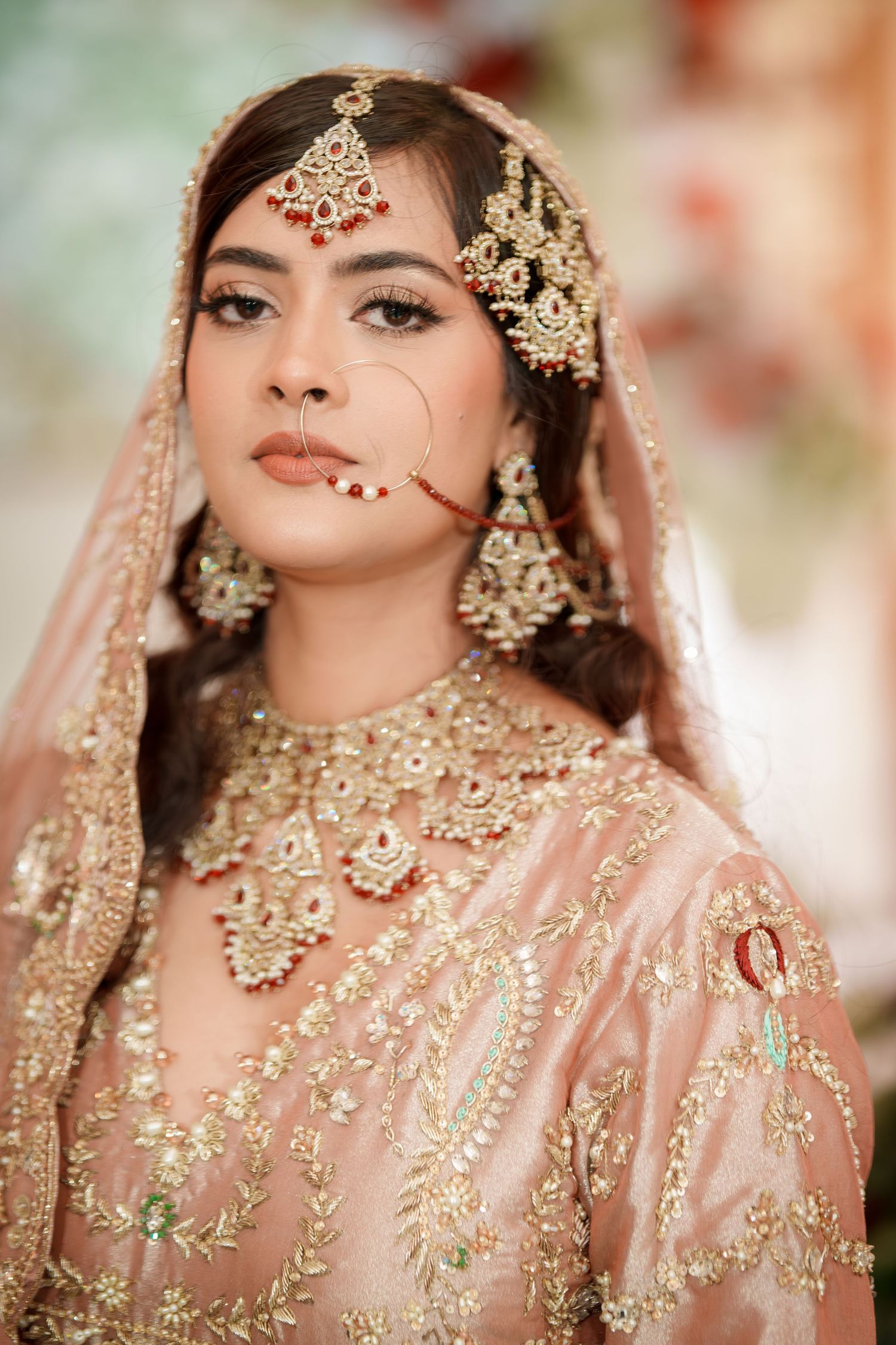 Close-up of bride wearing ornate gold jewelry and pink embroidered wedding attire.