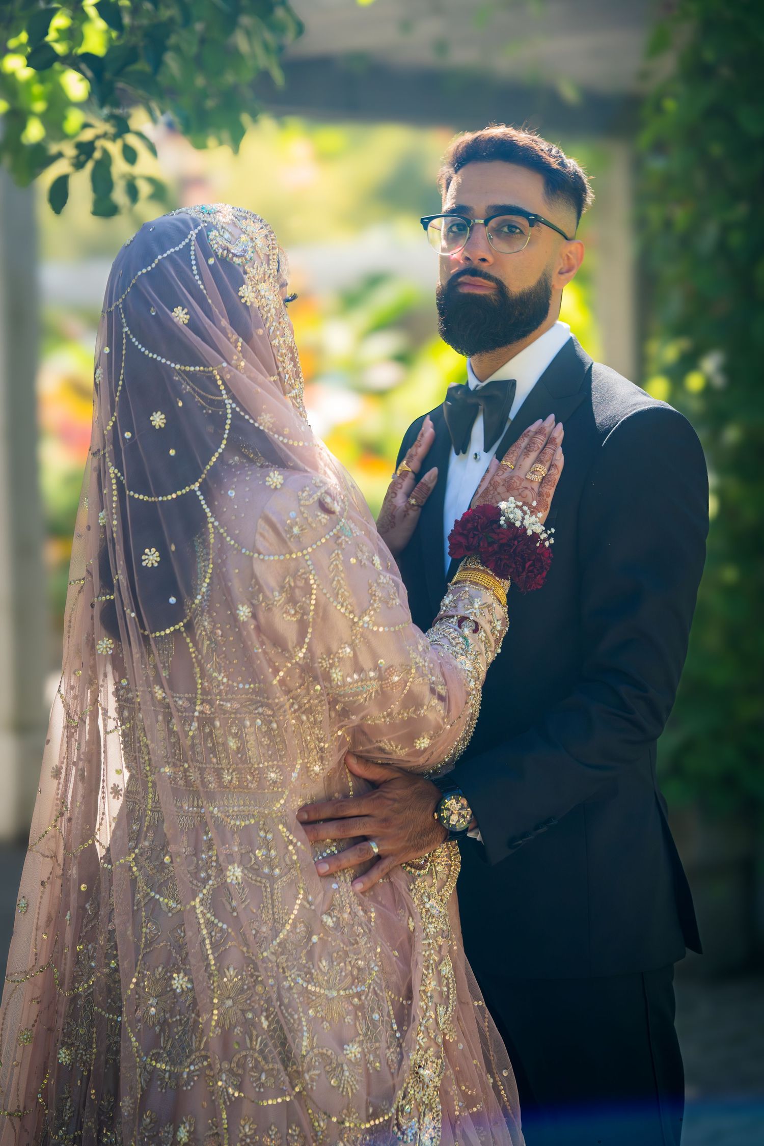 Elegant South Asian wedding couple embracing outdoors in traditional bridal attire with intricate details.