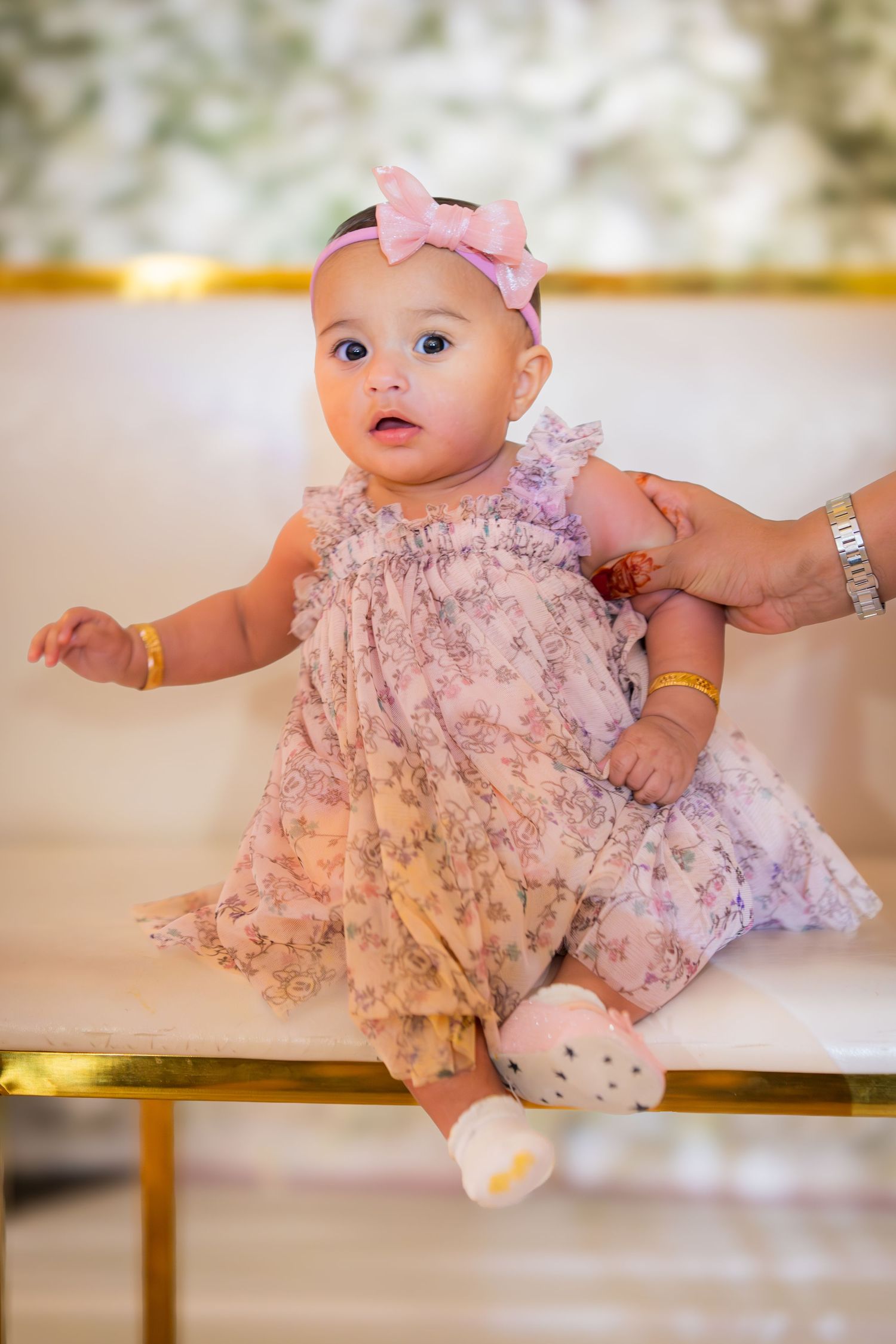 Baby in pink floral dress lying on white surface with multiple poses showing different angles and expressions.