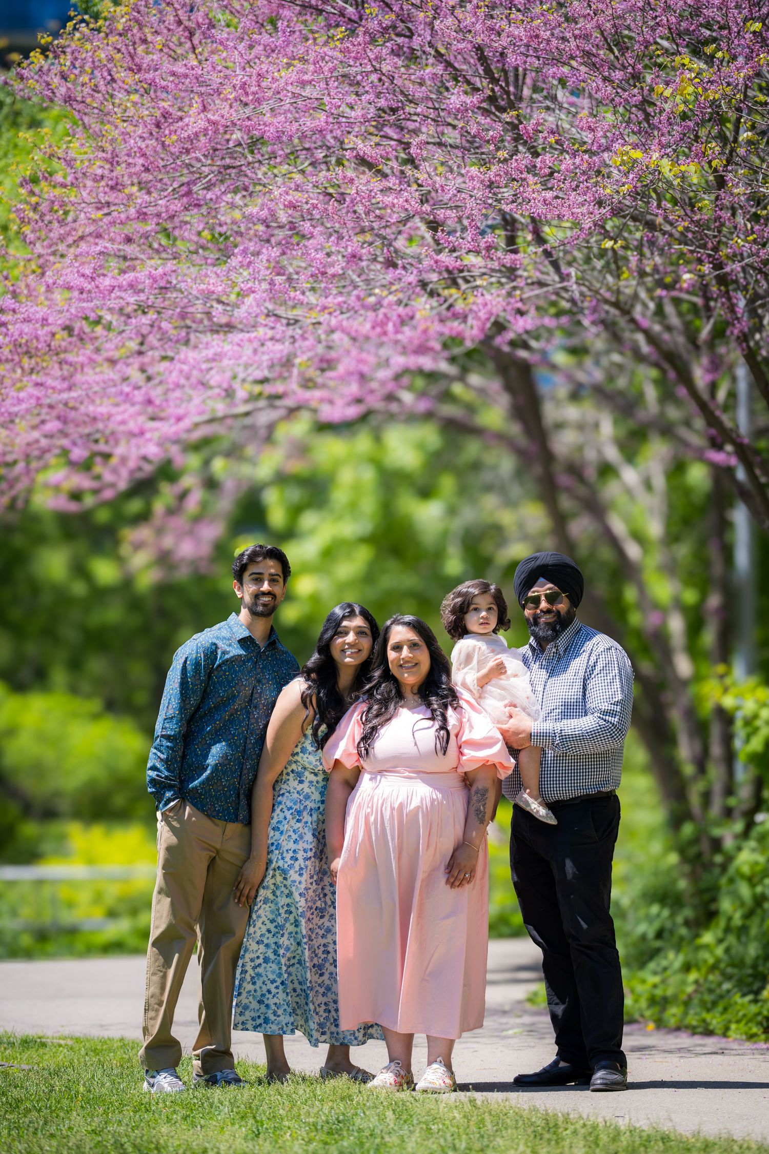 Happy family group portrait under flowering pink redbud trees in bright spring park.