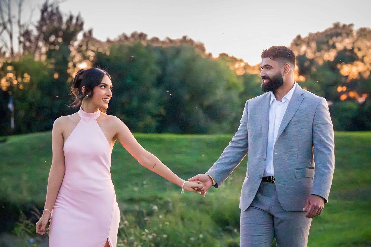 A couple walks together on a gravel path surrounded by lush greenery at sunset.