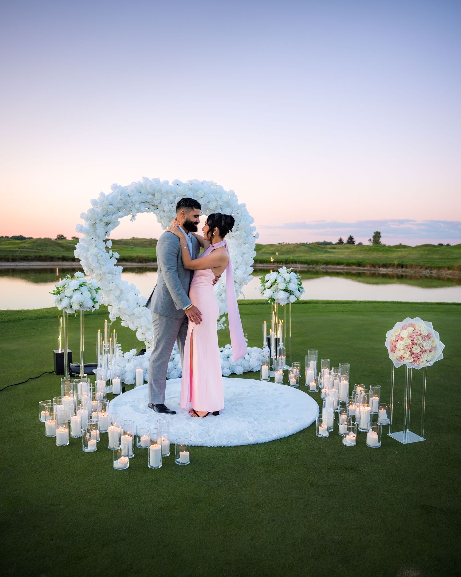 Intimate wedding ceremony on golf course with floral arch and candlelit lanterns at sunset.