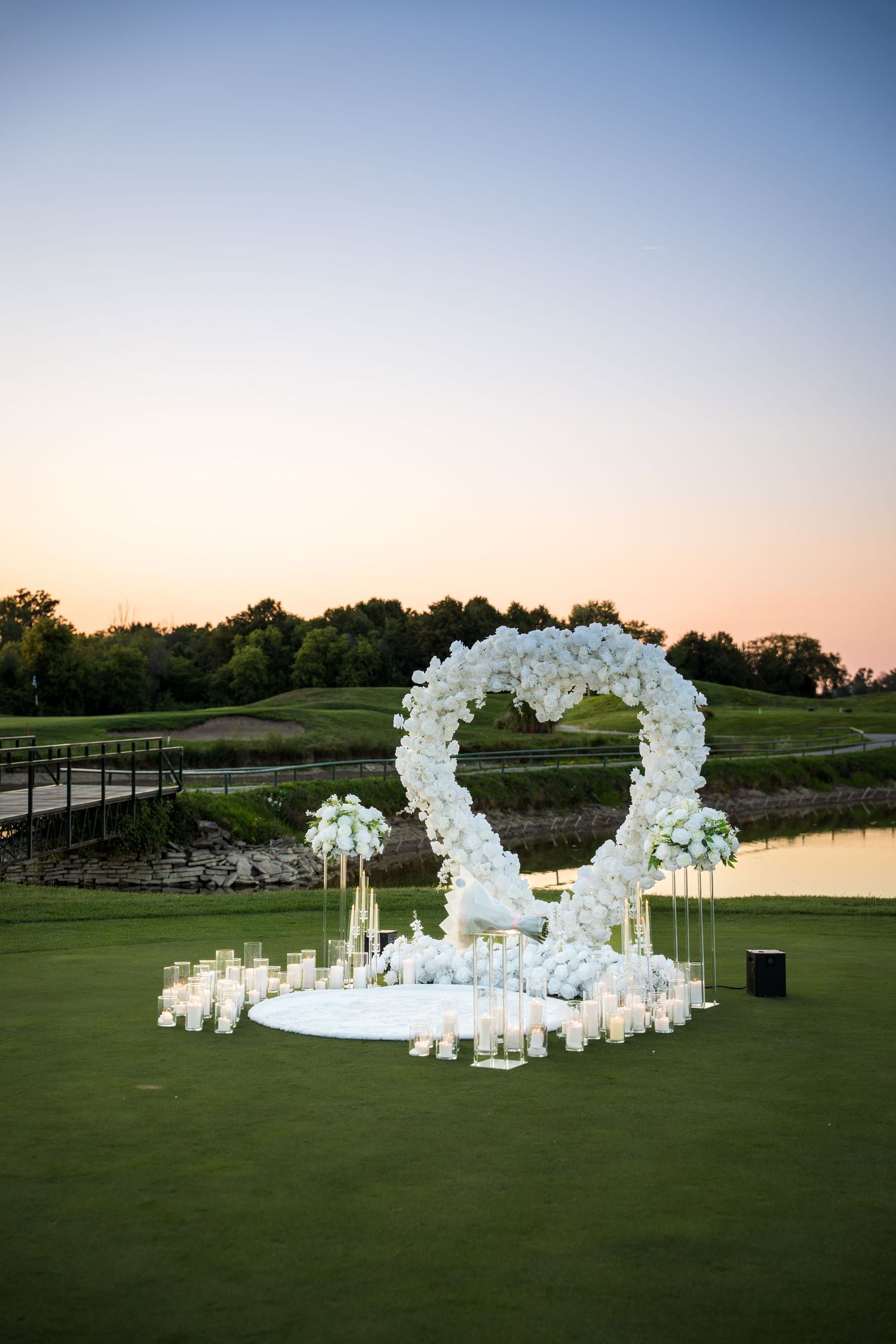 Stunning wedding ceremony setup with white floral arches and candles on manicured lawn.