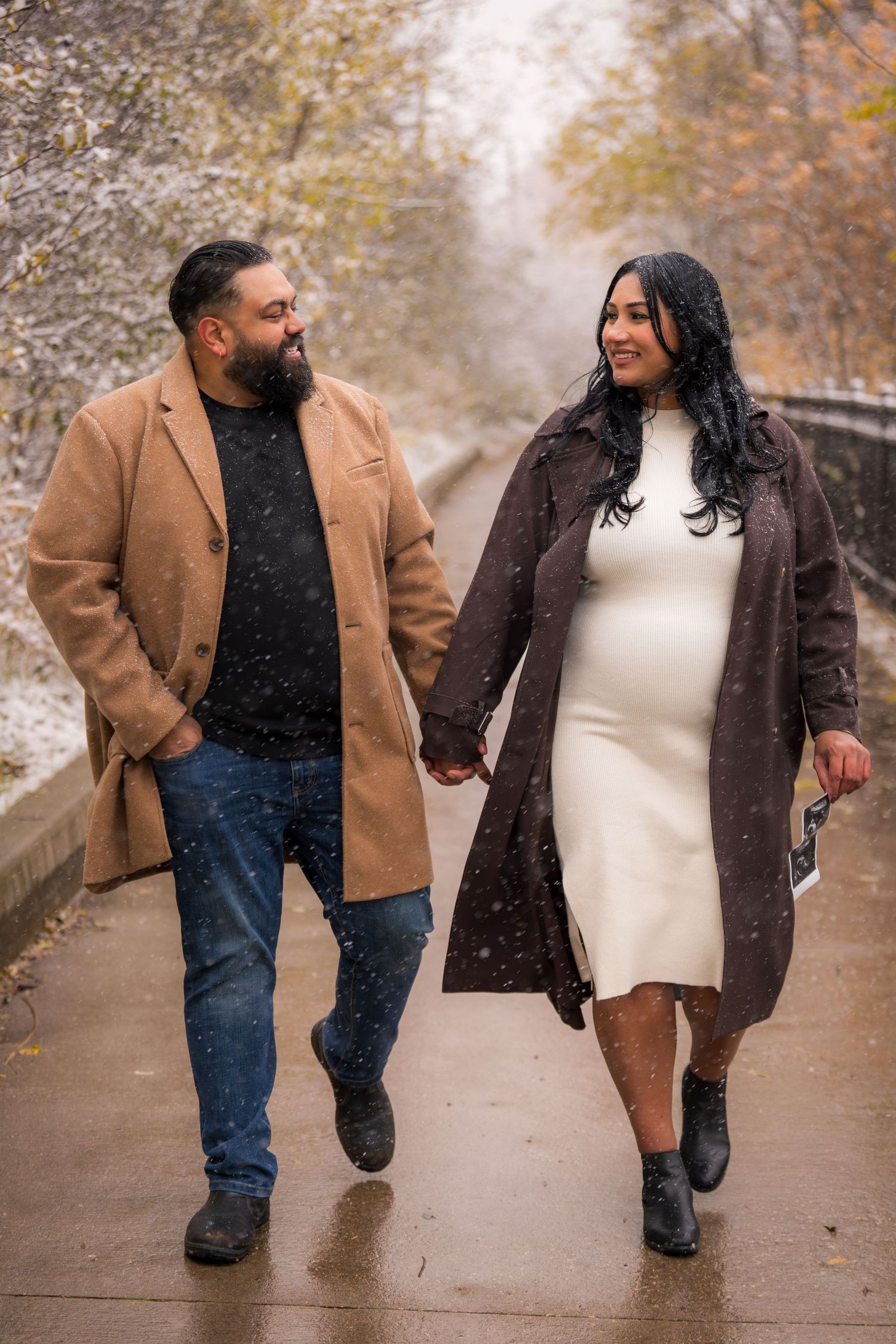 Couple walking hand in hand on path during light snowfall in autumn.