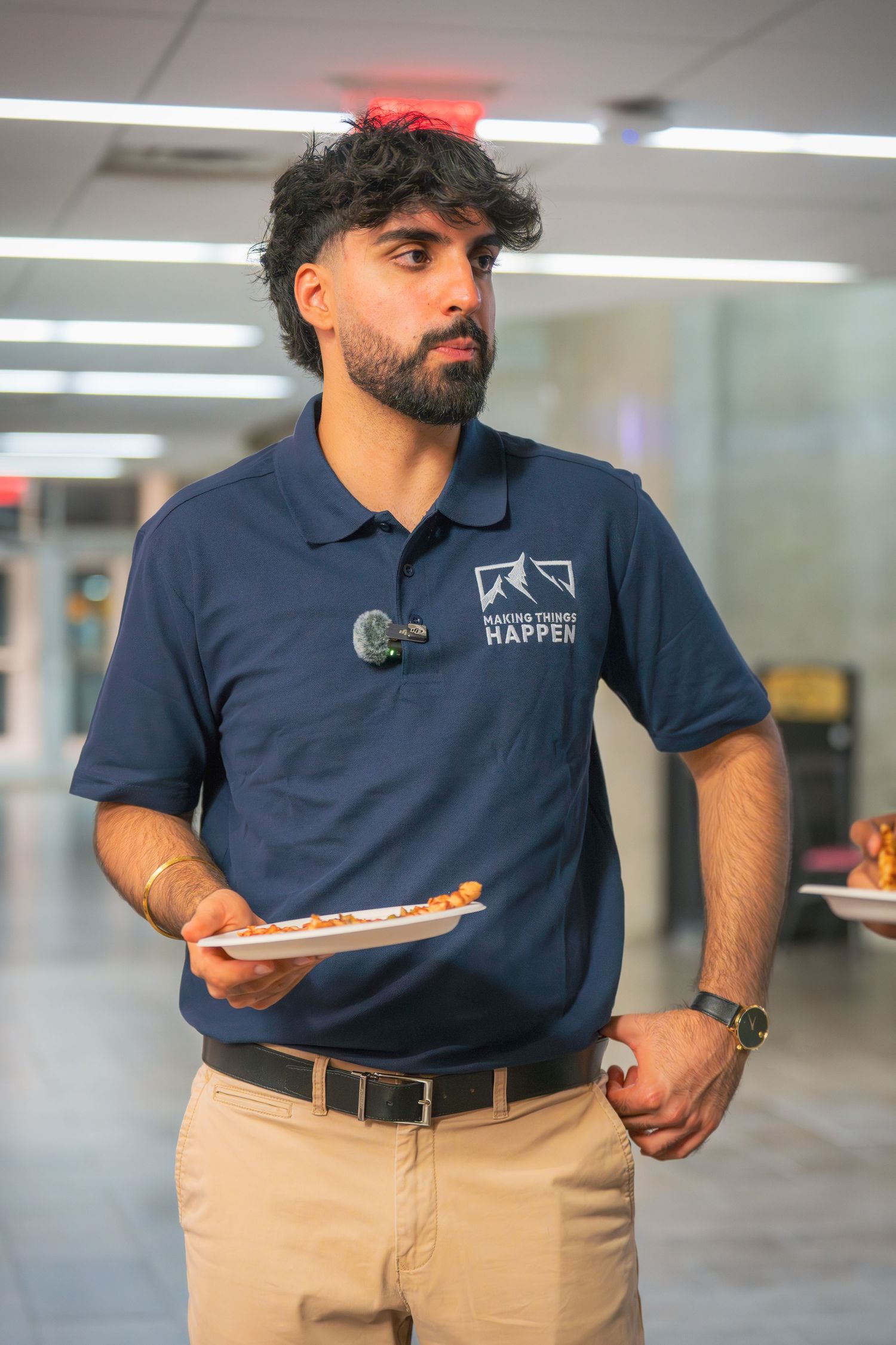 Person wearing a navy company polo and khaki pants stands presenting in an office environment.