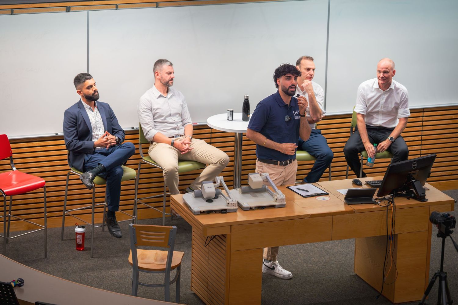 Professional panel discussion with speakers seated on wooden benches in a conference room.