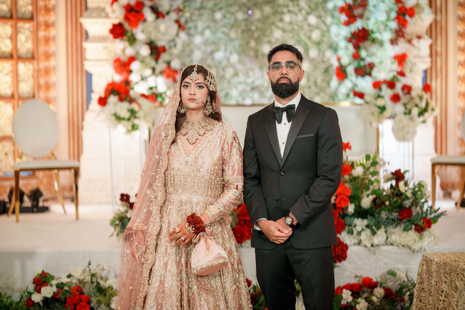Wedding portraits against a floral backdrop with red and white roses.