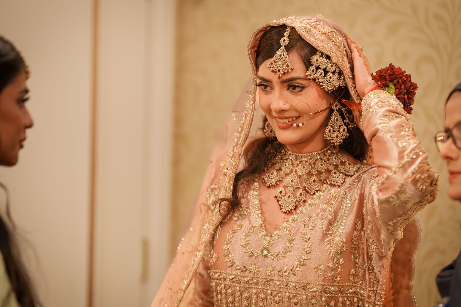 Bride wearing ornate pink embroidered lehenga and jewelry during traditional South Asian wedding ceremony.