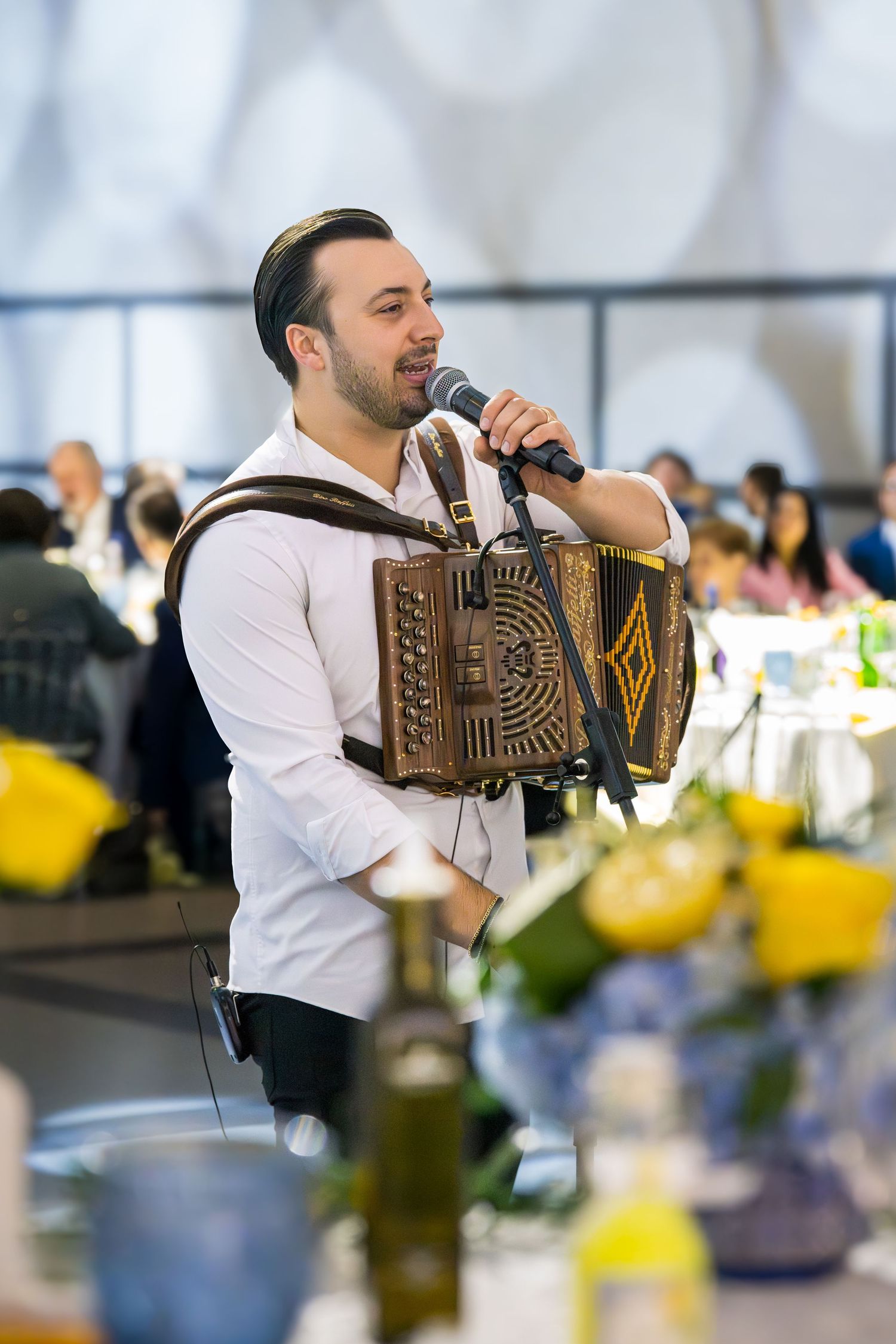 Male accordion player in white shirt performing and singing at a wedding reception banquet.