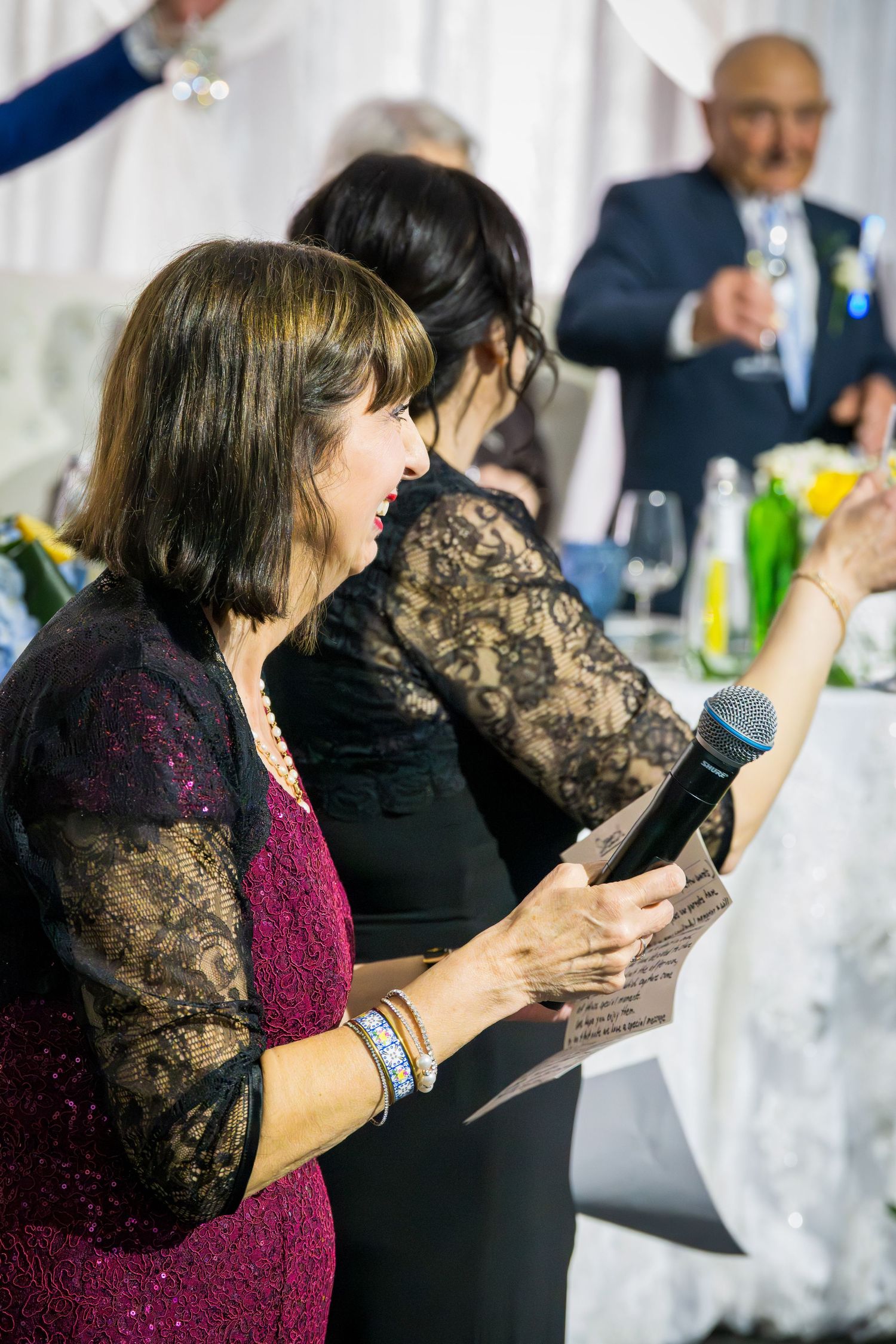 Woman in burgundy dress giving speech at wedding reception while holding microphone and notes.