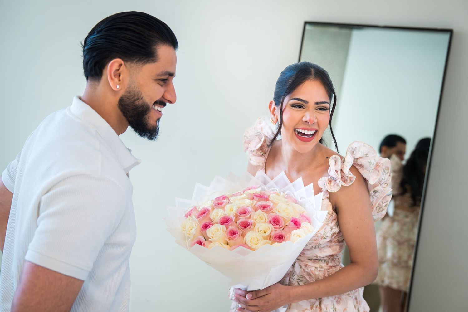 Man presenting woman with large bouquet of roses as she laughs with joy.