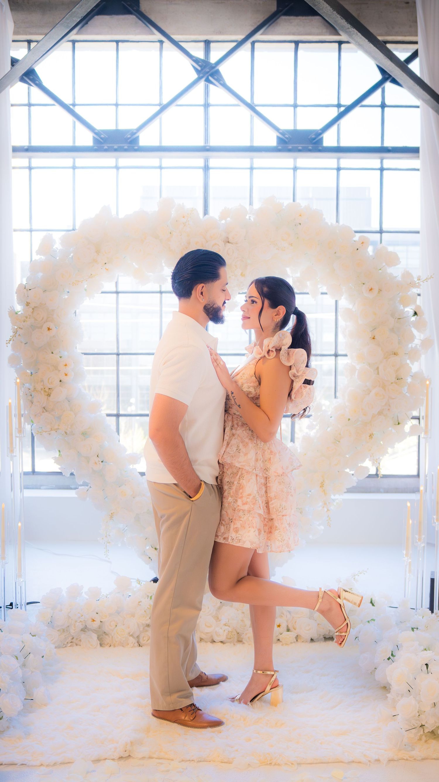 Couple gazing lovingly at each other framed by a large white floral heart arch.