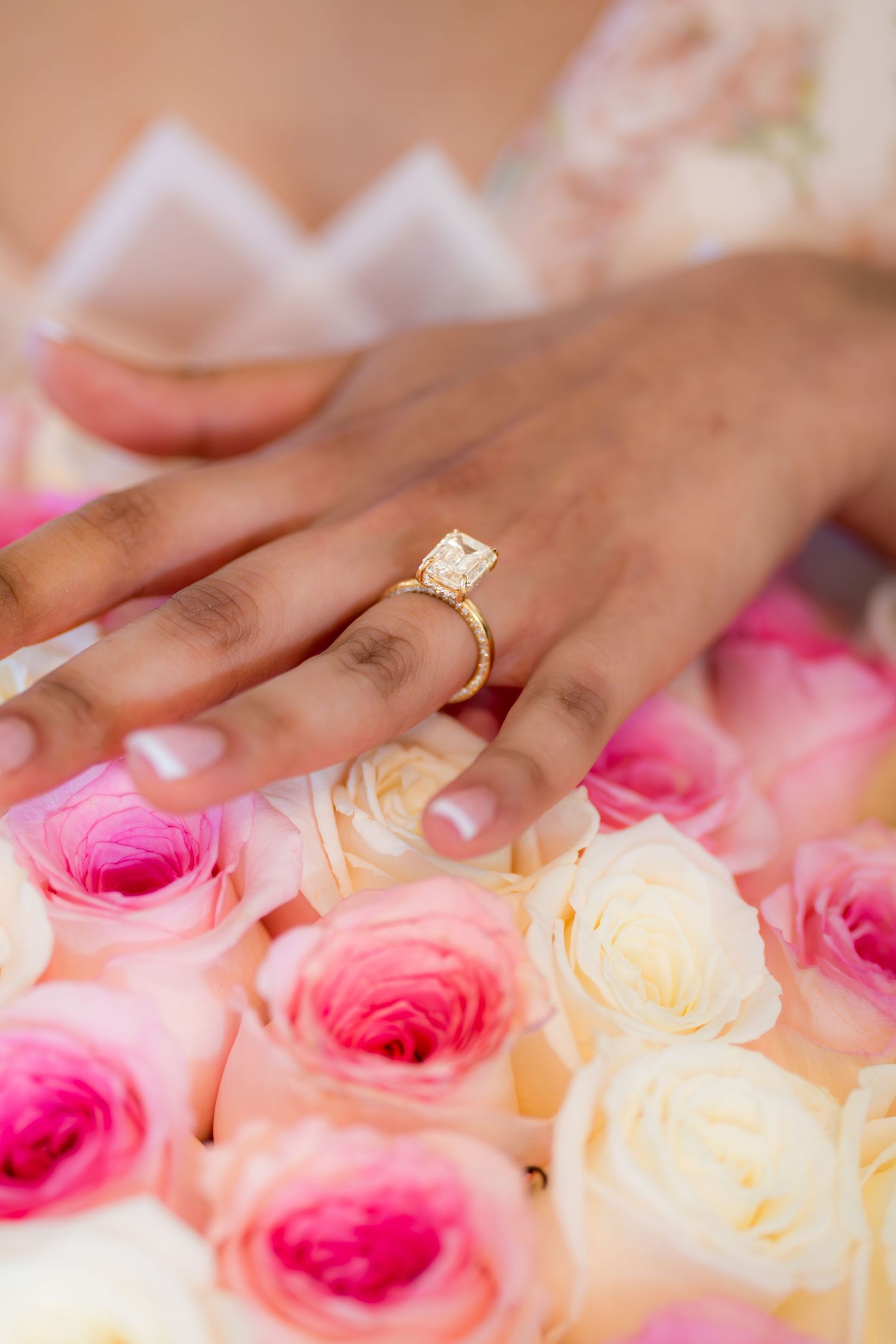 Close-up of engagement ring with cushion-cut diamond in gold setting displayed on hand over pink roses.