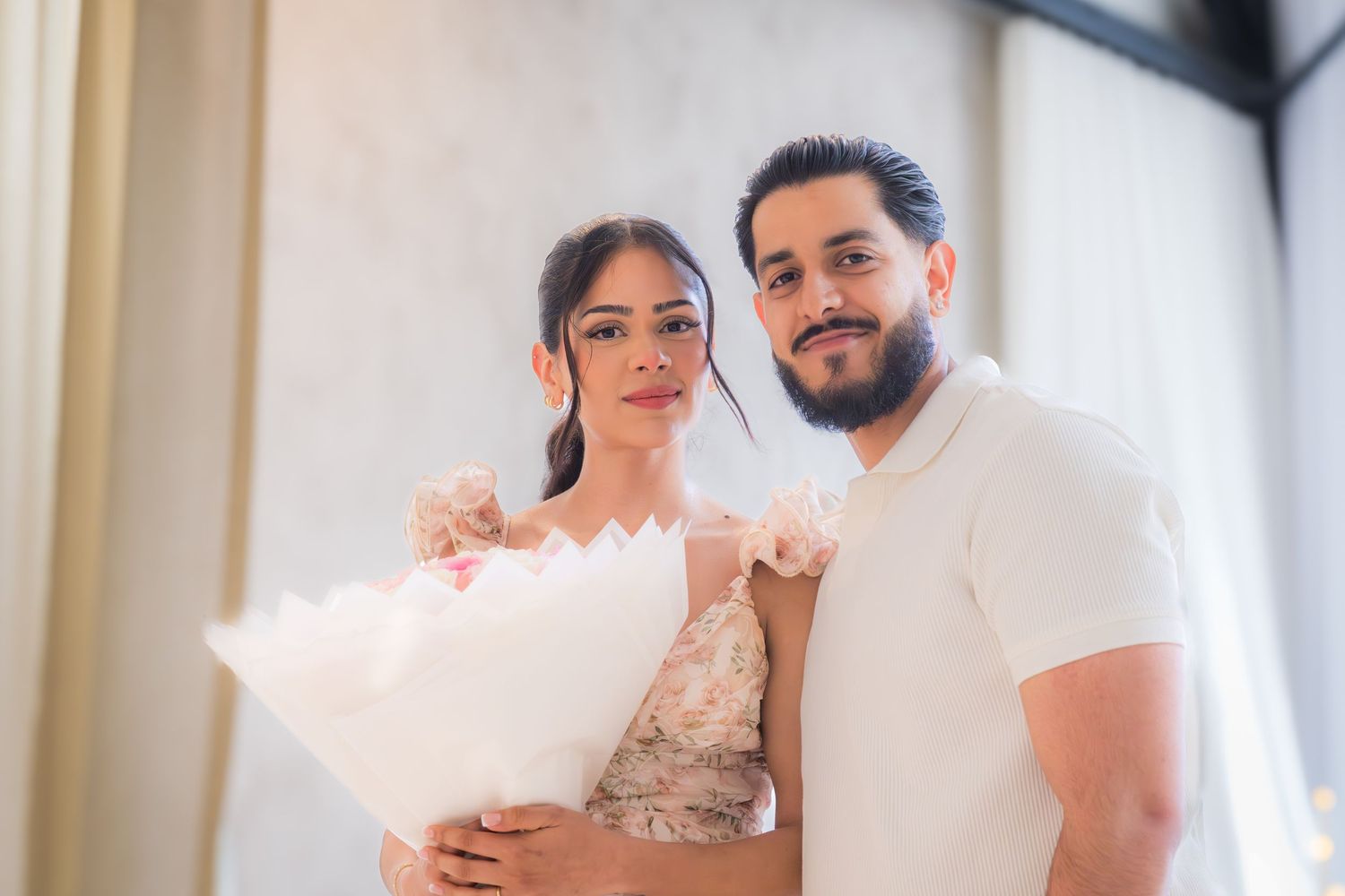 Newly engaged couple smiling together holding a white bouquet after a romantic proposal.