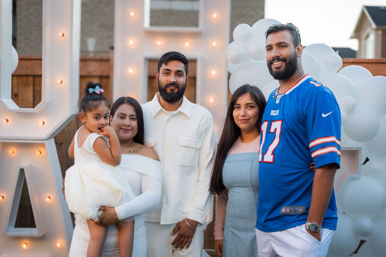 Group of five people posing together at outdoor gender reveal party with illuminated letter decorations.
