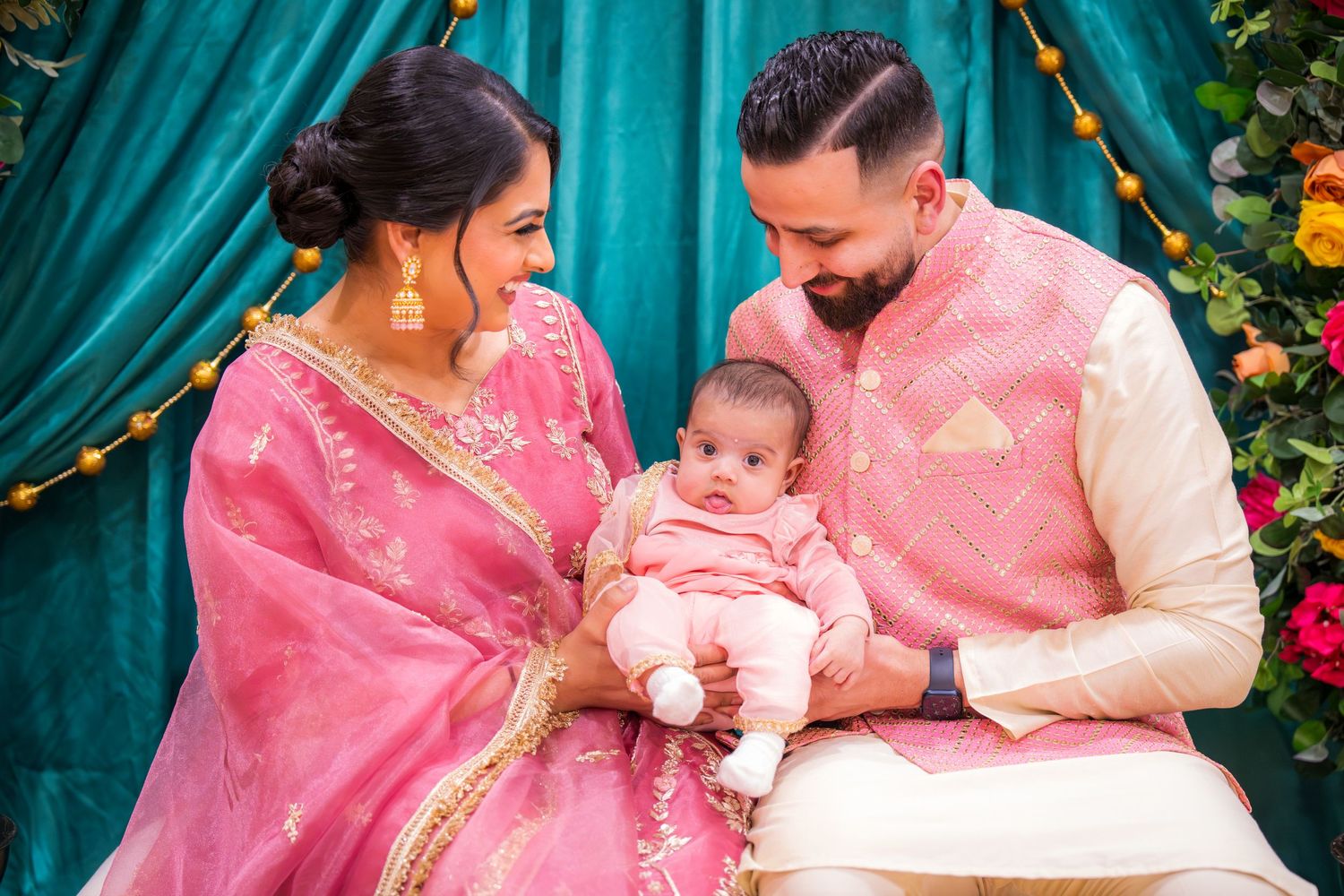 A couple in pink Indian traditional wear gazes lovingly at their newborn baby during a cultural ceremony.
