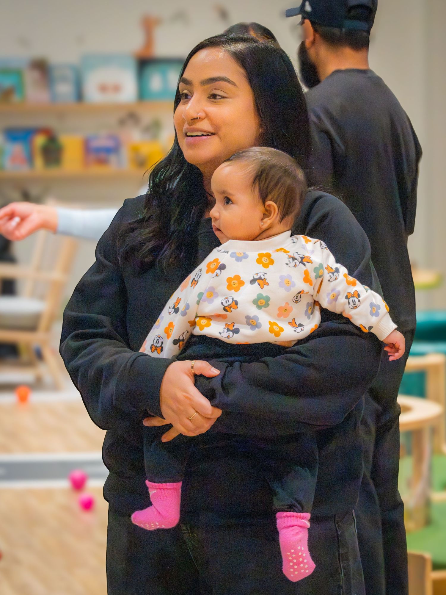 Woman in black hoodie holding a baby dressed in floral onesie with pink socks.