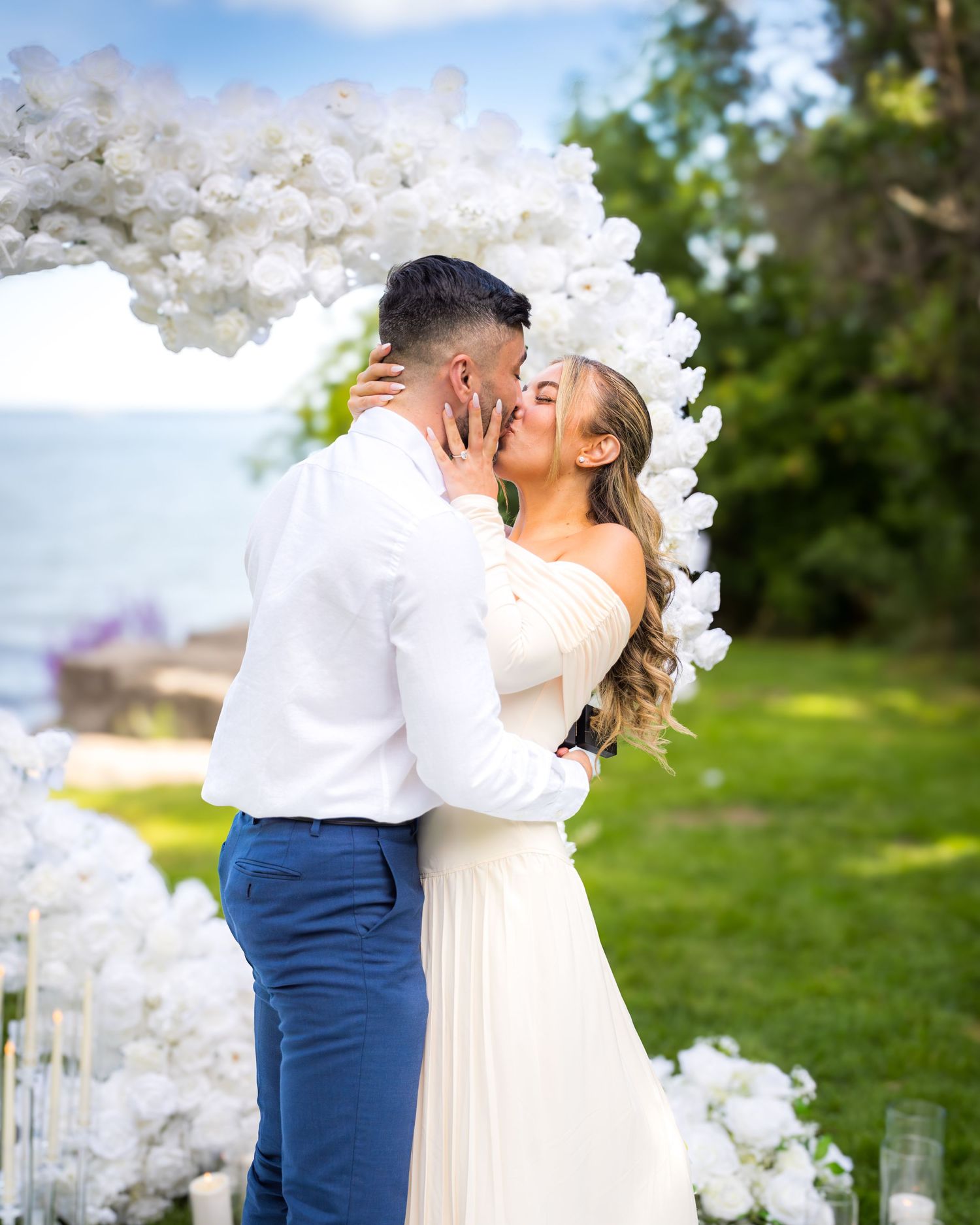 Intimate proposal scene with white floral arch and candlelit decorations in outdoor setting.