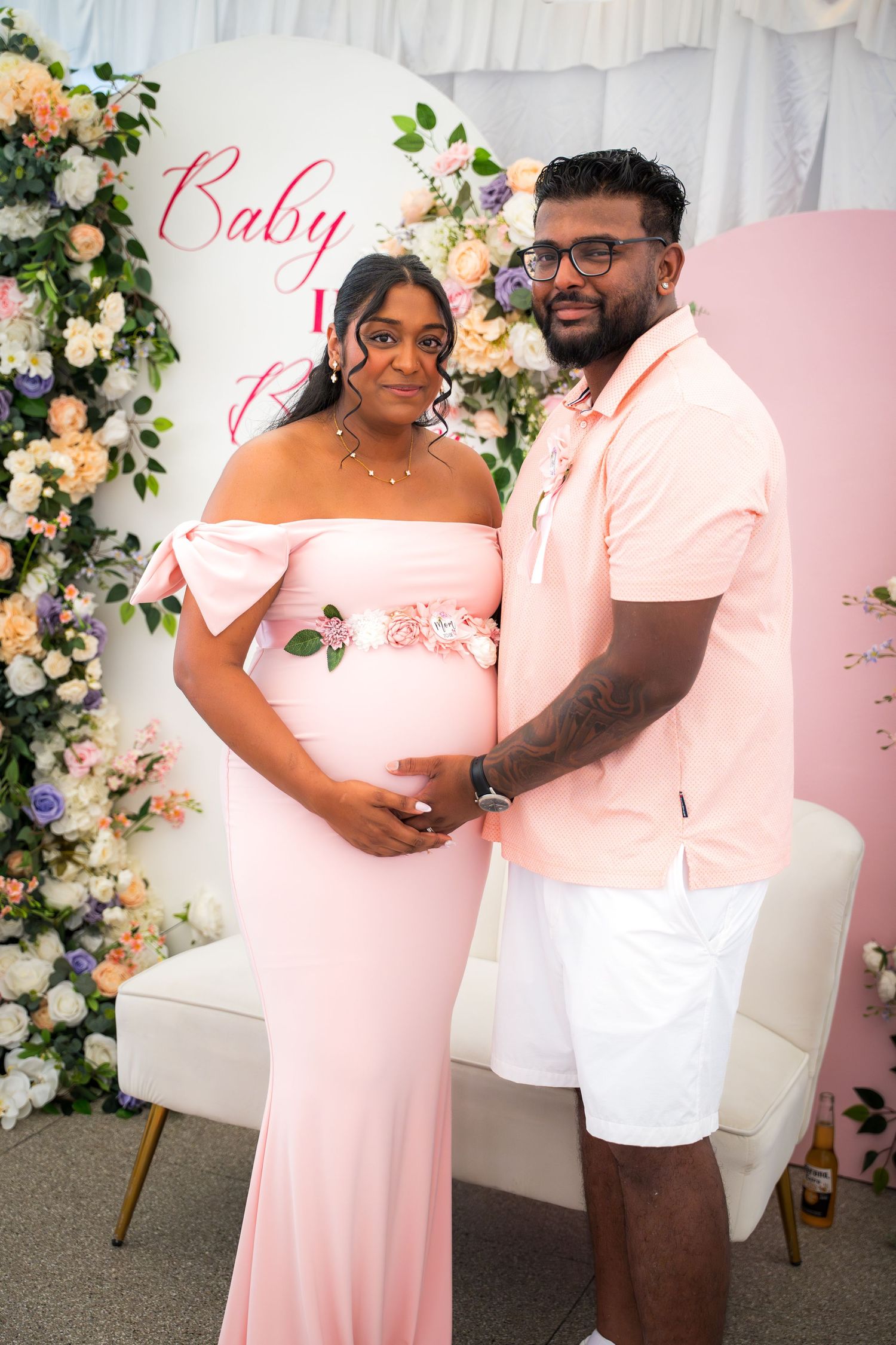 Elegant baby shower photo session with pink dress and floral backdrop.