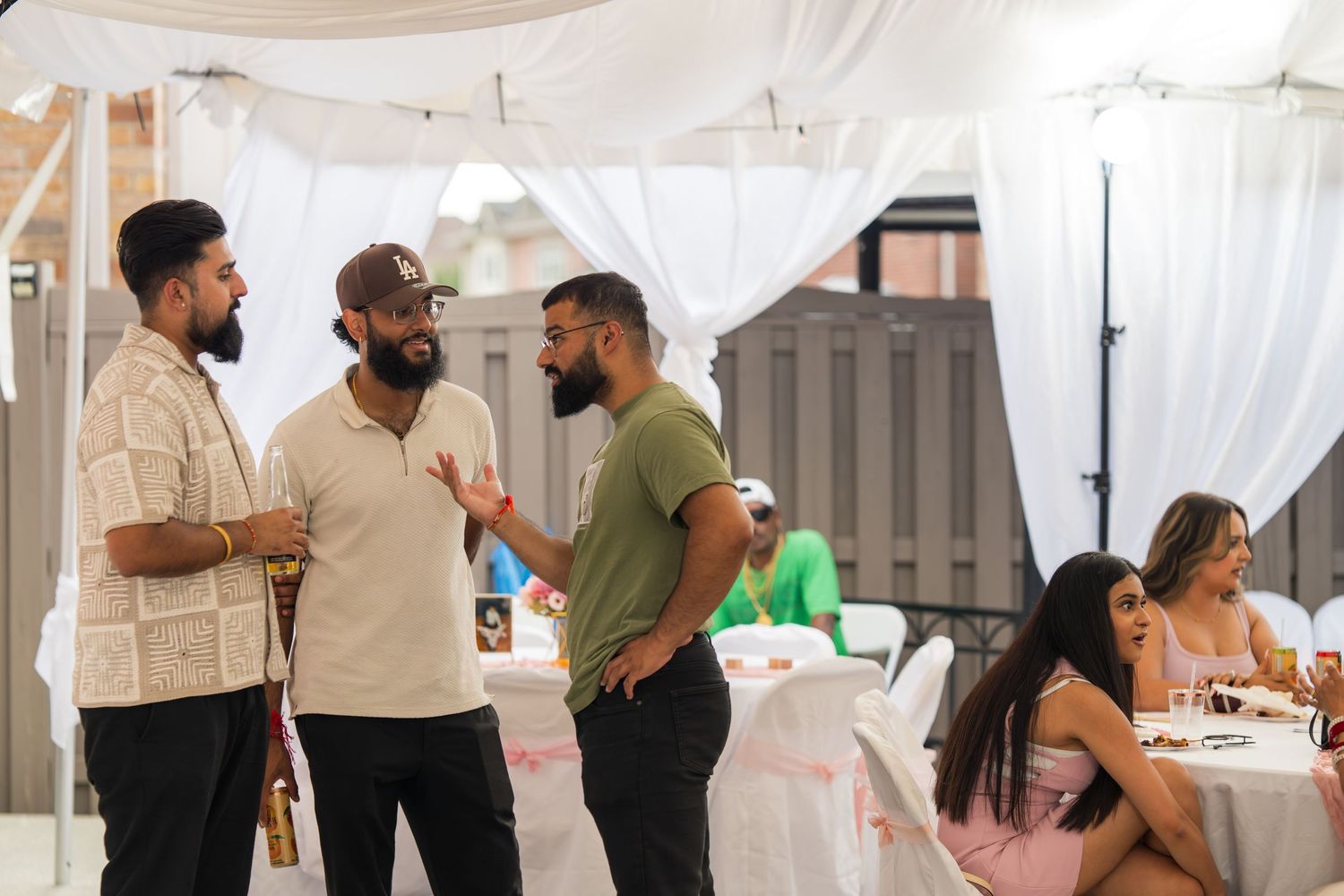A group of people chatting at an outdoor event with white tent draping.