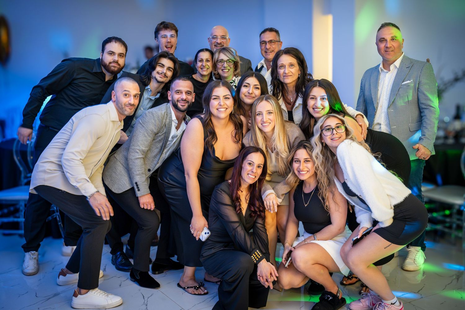 Group of friends posing together at a party with colorful lighting in the background.