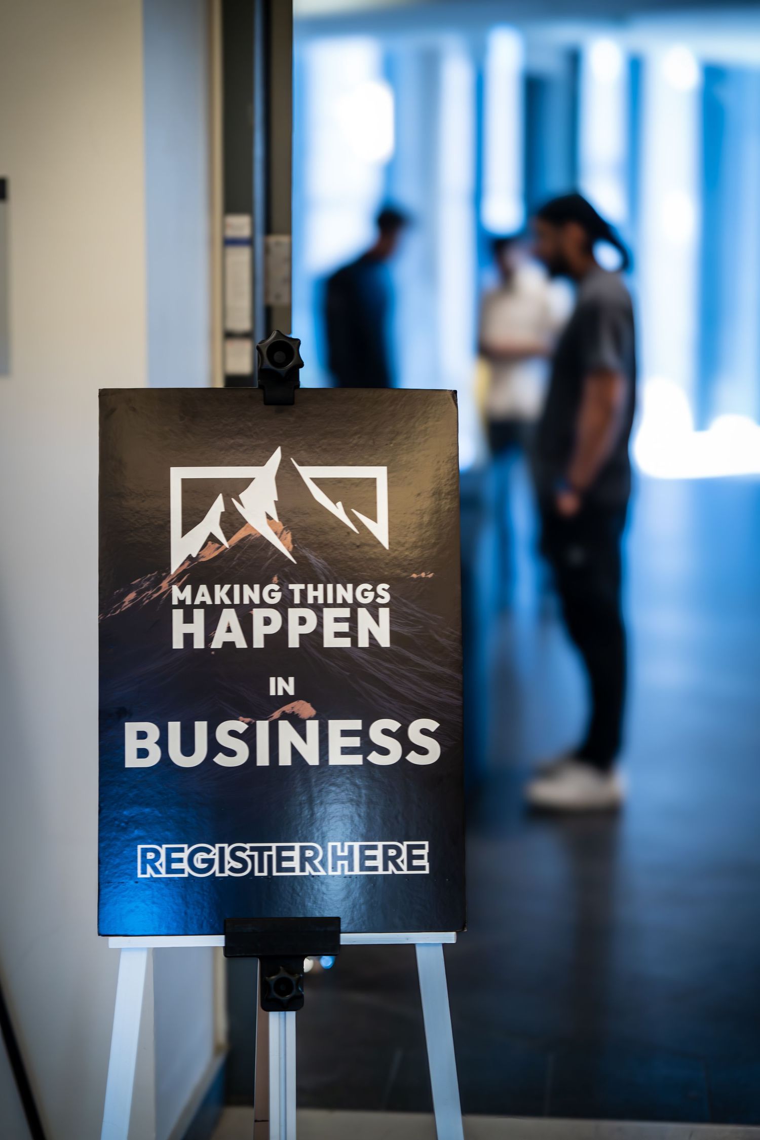 Conference signage reading 'Making Things Happen in Business' displayed on dark stands with blue lighting.