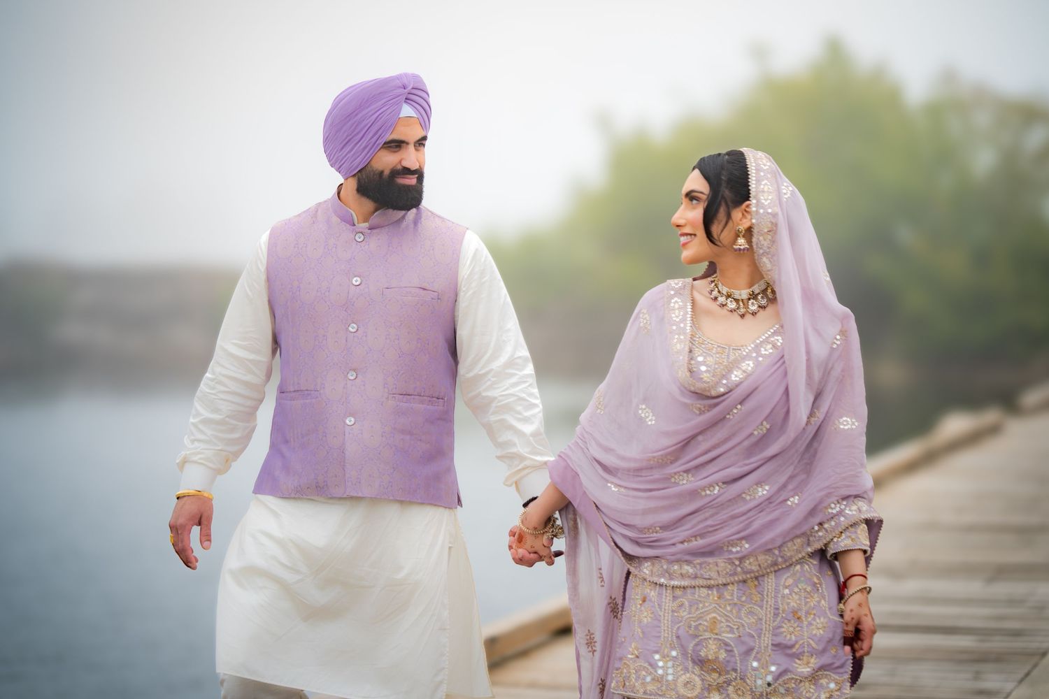 Traditional Punjabi wedding couple walking together in matching purple and white outfits.