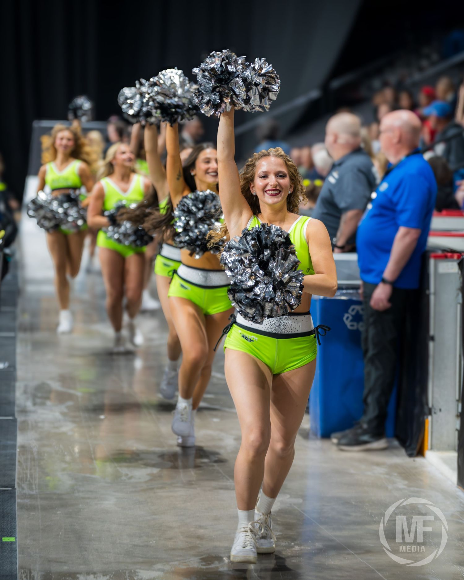 Cheerleaders in neon green uniforms with silver pom-poms perform at a Niagara basketball game.