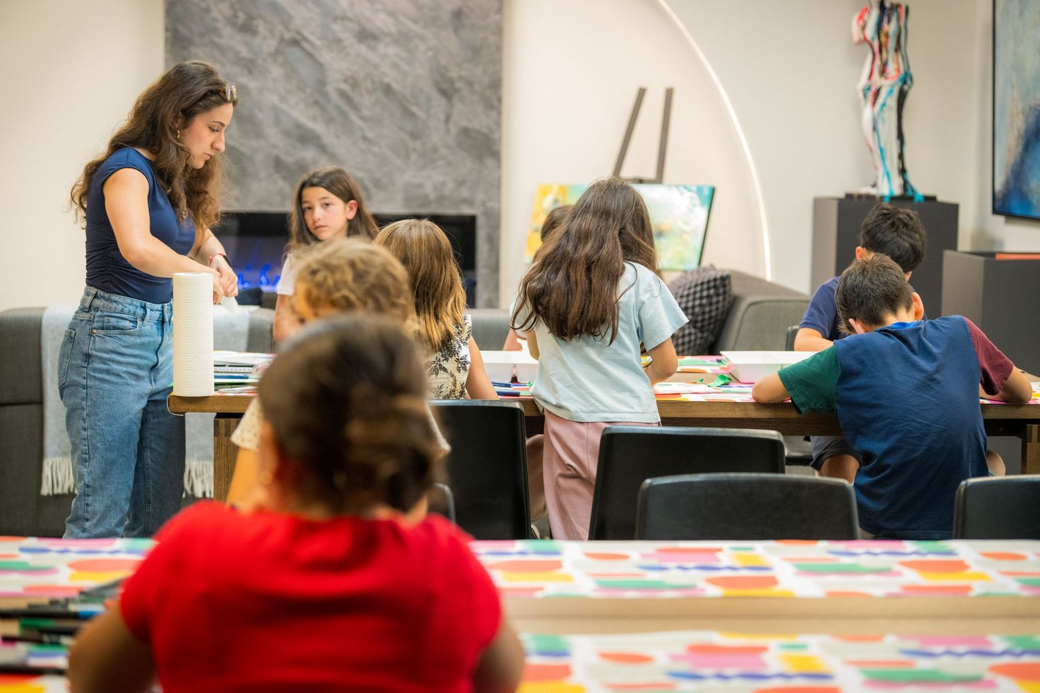 Teacher assists children during an art class activity in a modern classroom setting.