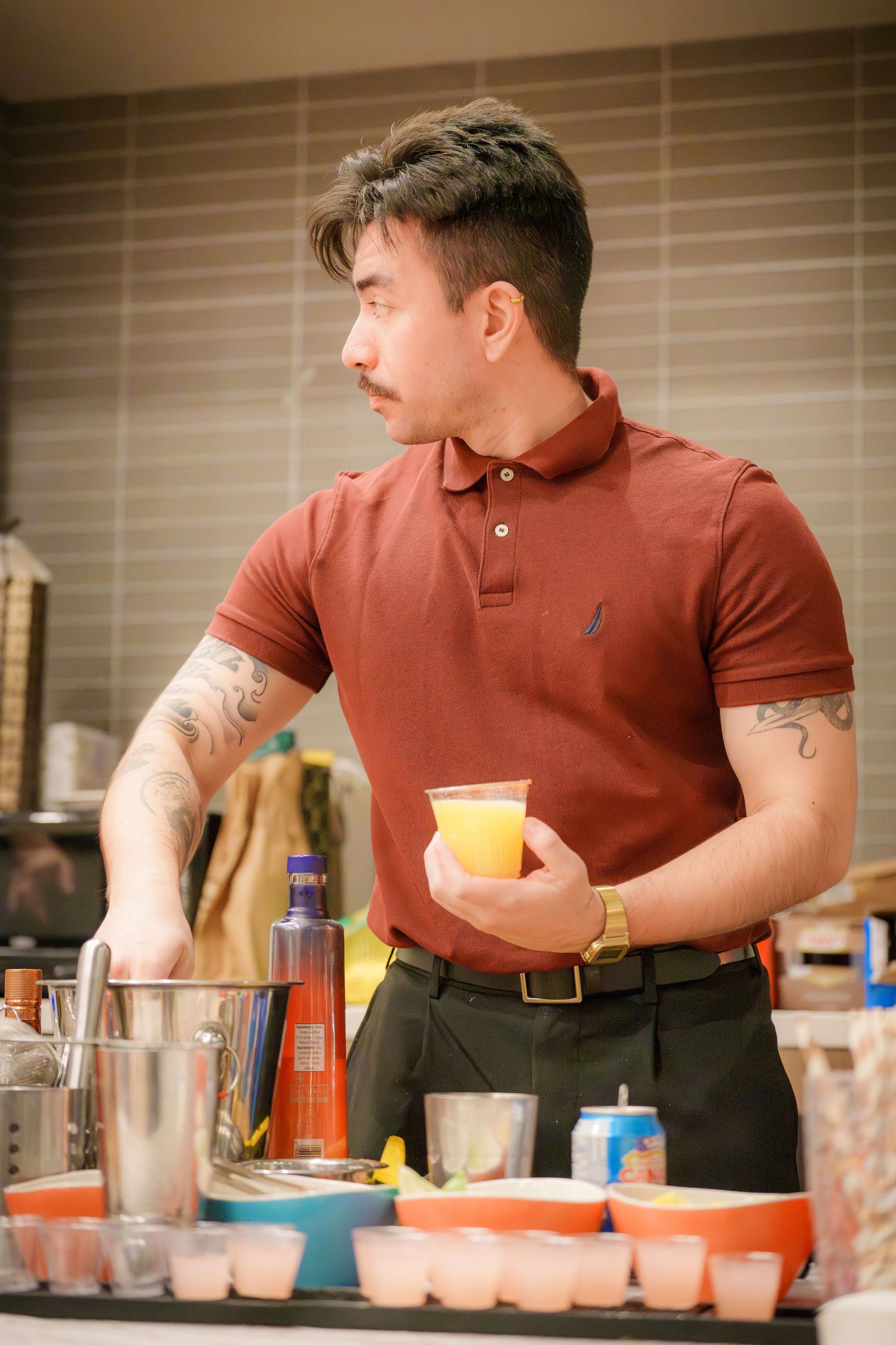 A person in a red polo shirt stands at a table with drinks and cups during what appears to be a party setting.