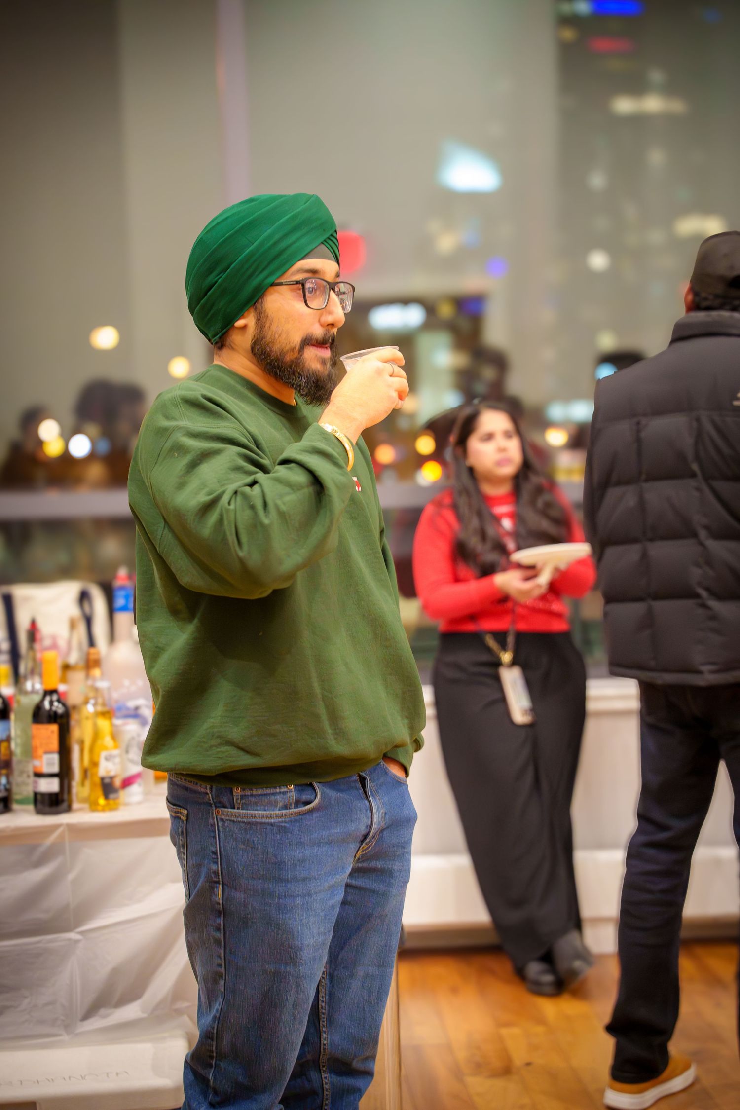 Person in a green hoodie and jeans playing beer pong at an indoor party.