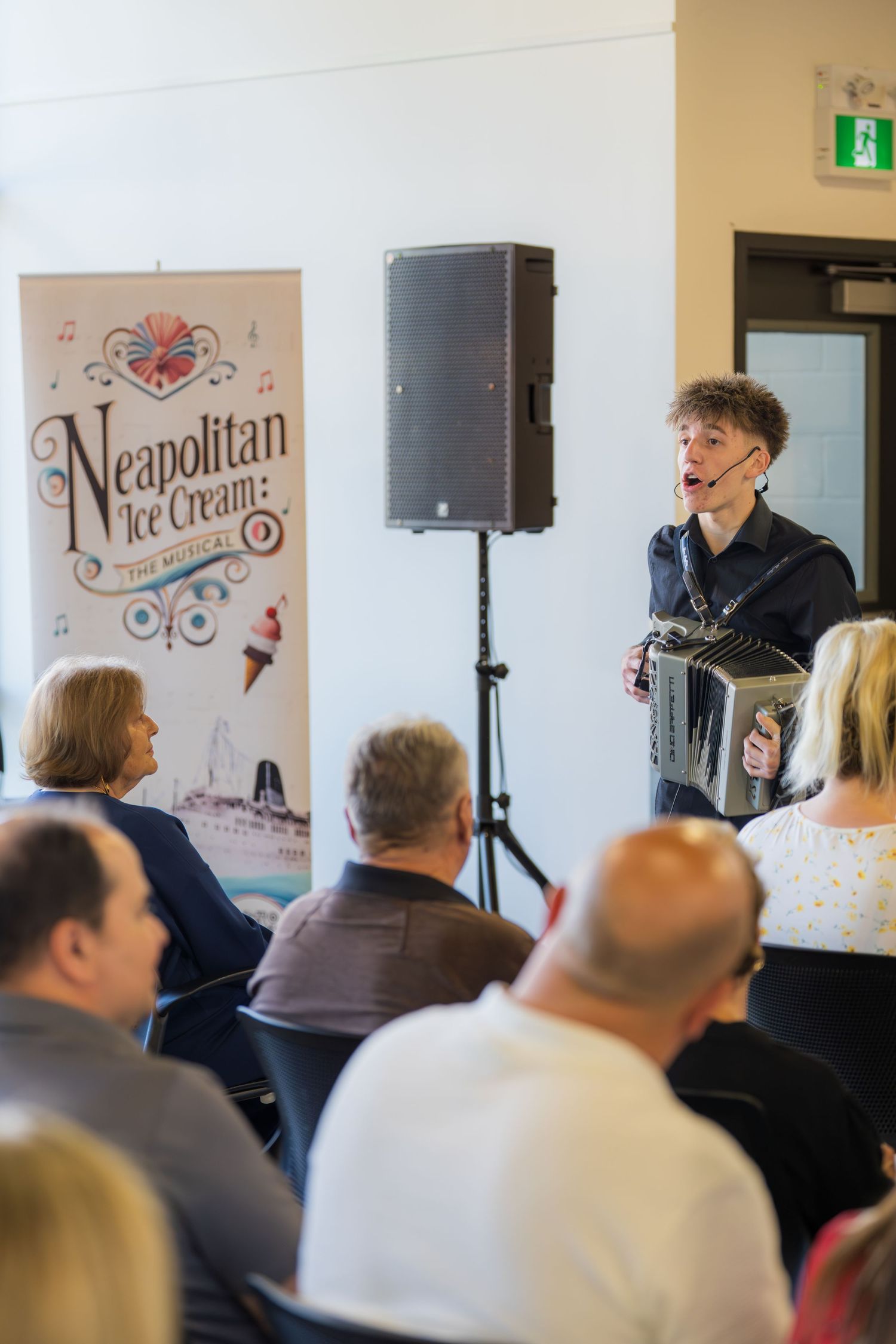 Young musician plays accordion at Neapolitan Ice Cream The Musical promotional event for seated audience.