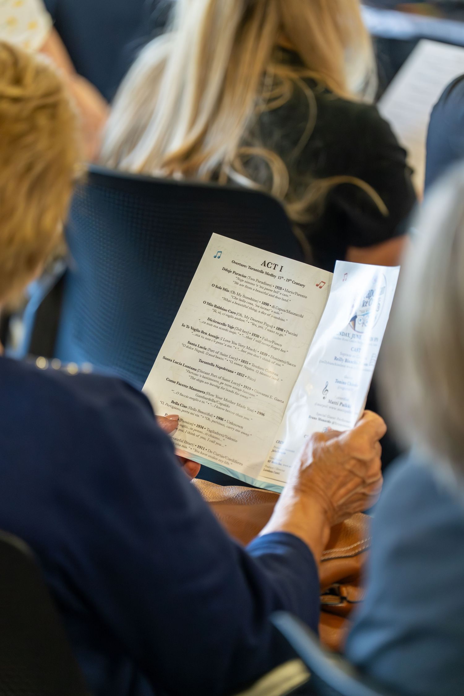 Audience member reading ACT 1 program at formal Italian cultural performance event.