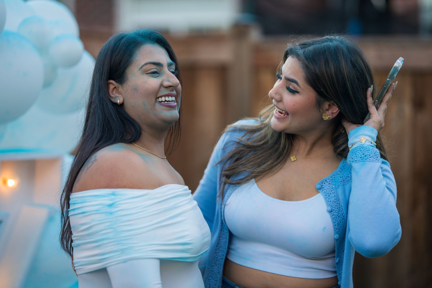 Two young women laughing and smiling together at an outdoor baby shower celebration.