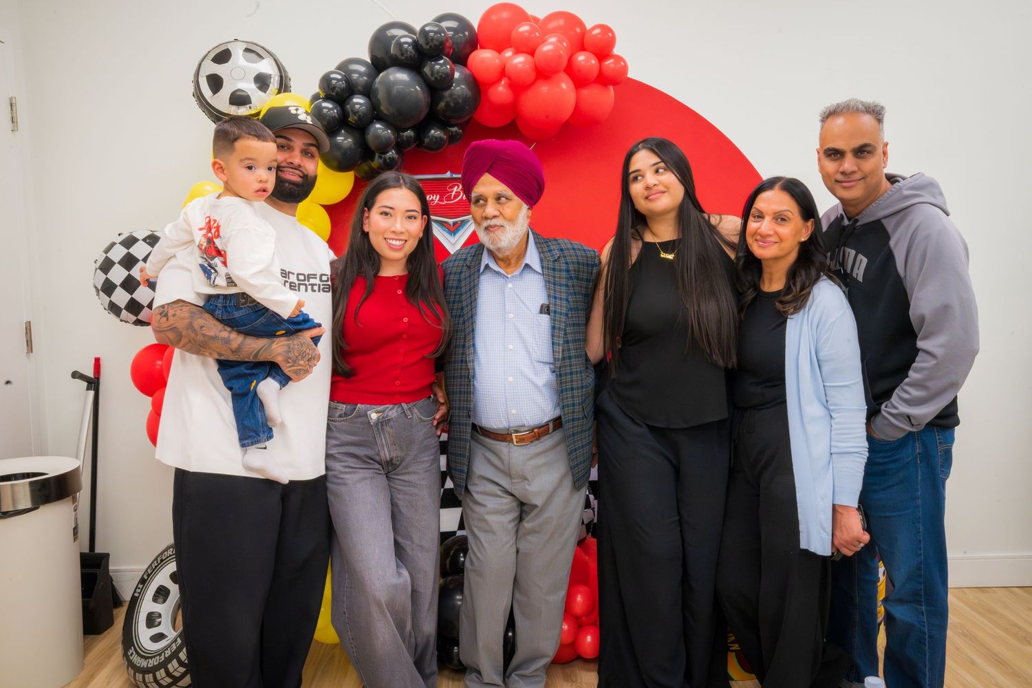 Family group of seven posing in front of red Cars movie balloon arch at a birthday party celebration.