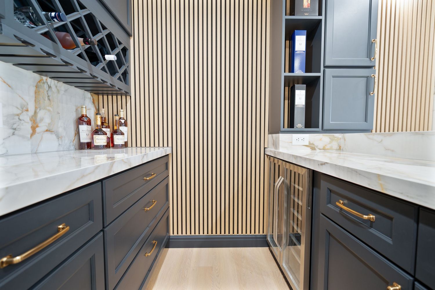 Modern kitchen features navy blue cabinets, vertical wood slat walls, and white marble countertops with gold hardware accents.