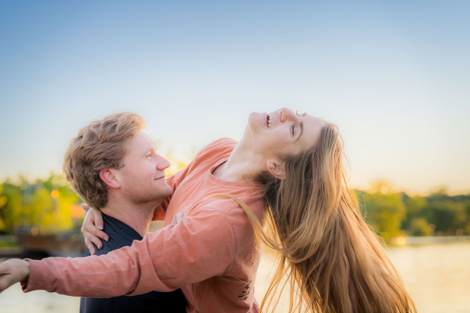 Joyful couple embracing outdoors at golden hour with a clear sky background.
