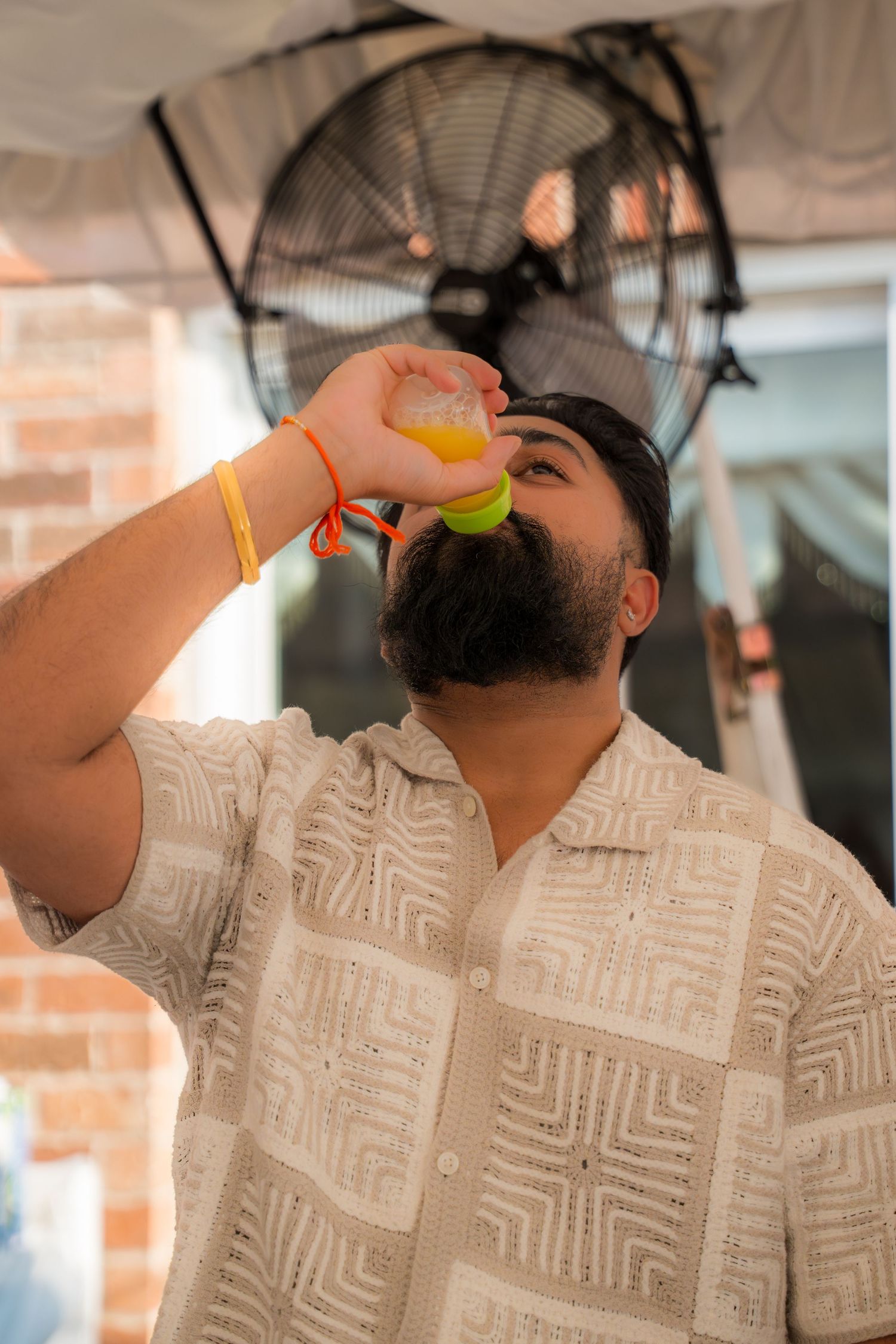Person in white patterned shirt drinking a beverage against brick wall background.
