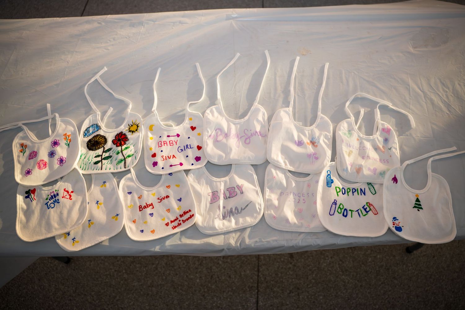 Long line of decorated white baby bibs displayed on dark floor with artistic designs.