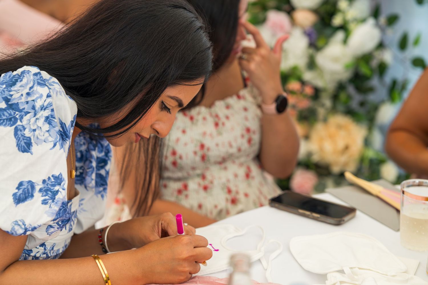 People gathered around tables at a social event with floral centerpieces and white tablecloths.