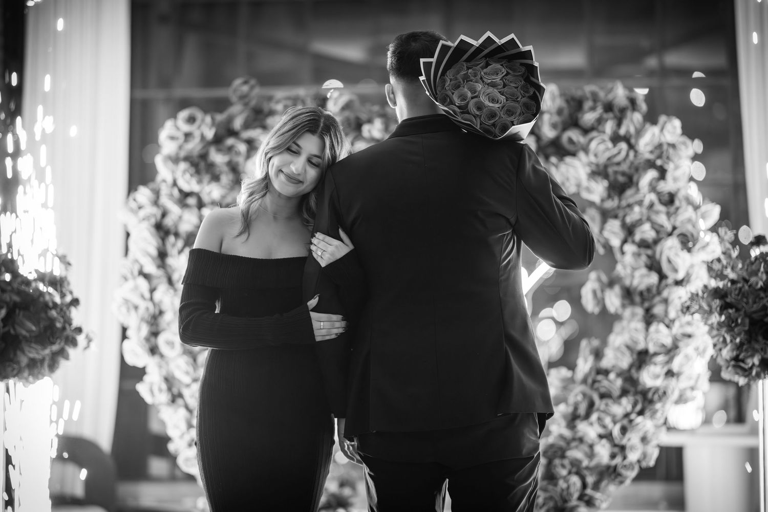 A black and white photo of a couple dancing together surrounded by floral decorations.