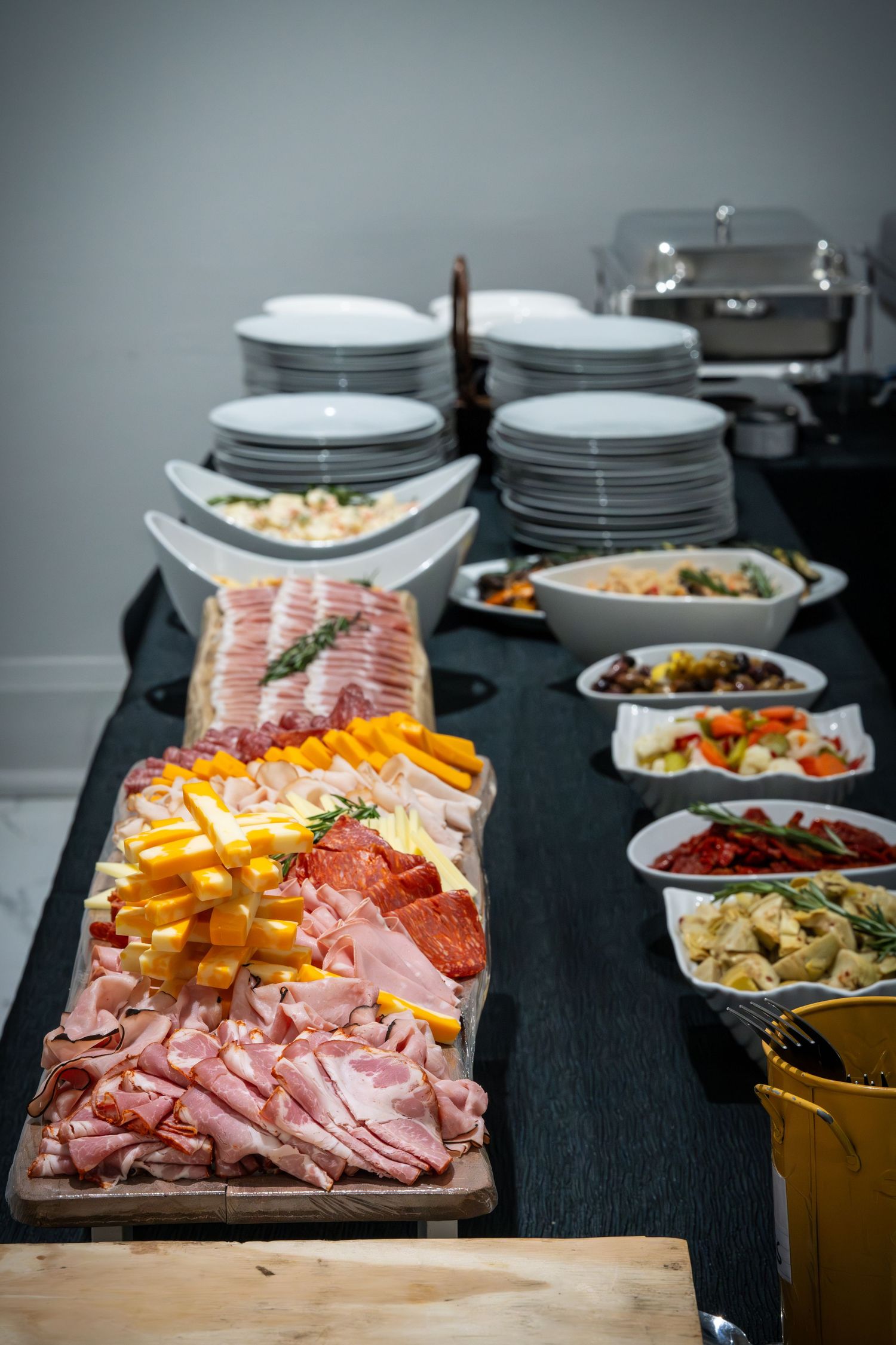 Charcuterie board with sliced meats, cheeses and colorful appetizers arranged on a dark tablecloth.