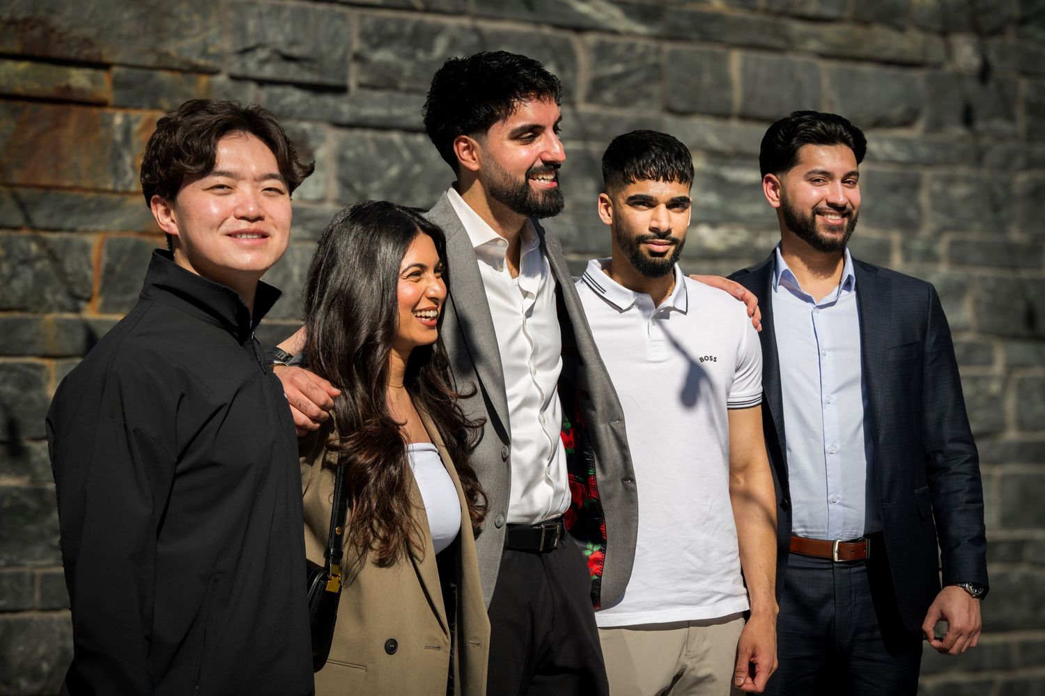 Group of people posing together outdoors against a stone wall.