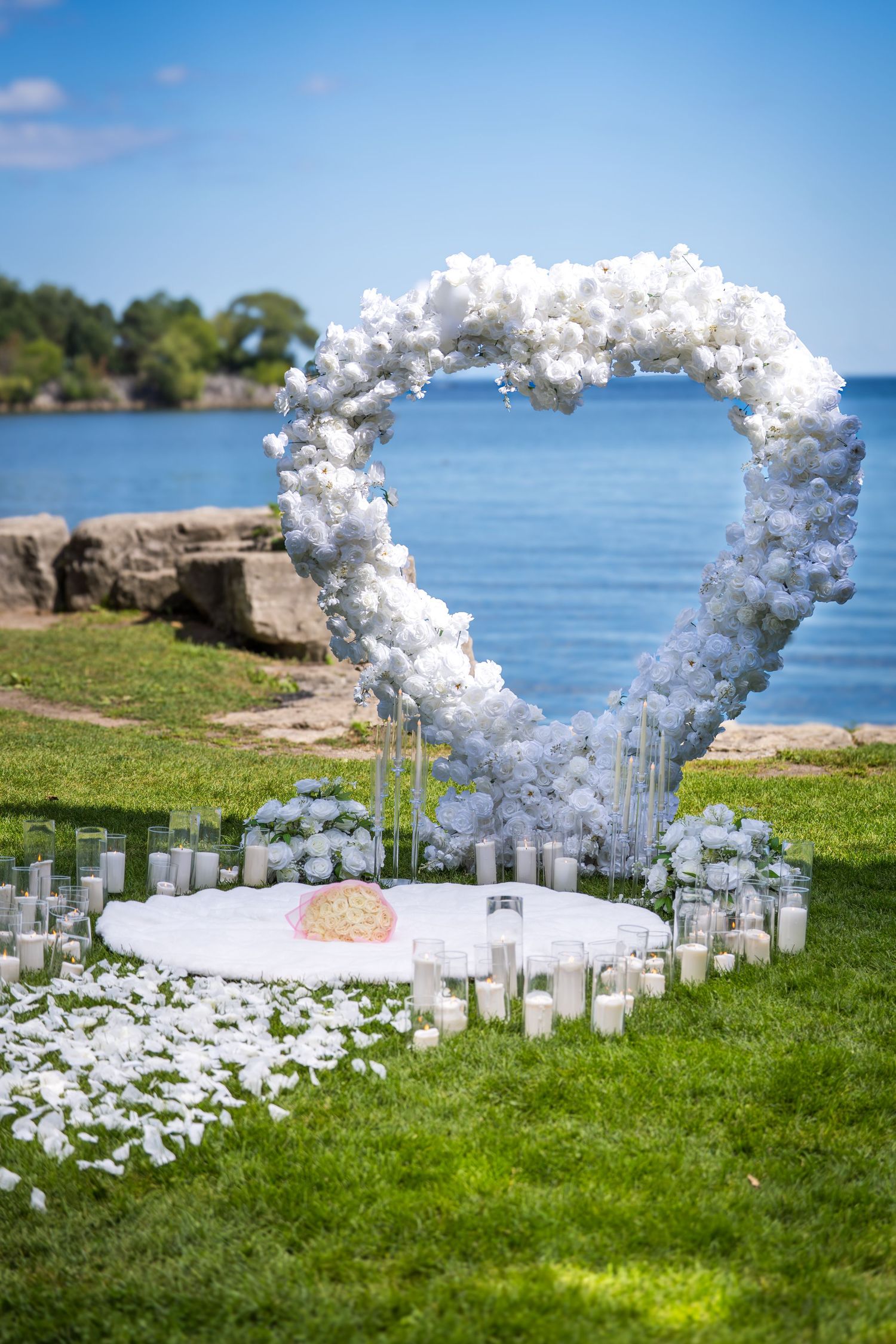 Outdoor wedding setup featuring a white floral arch and candles on a grassy cliff overlooking the ocean.