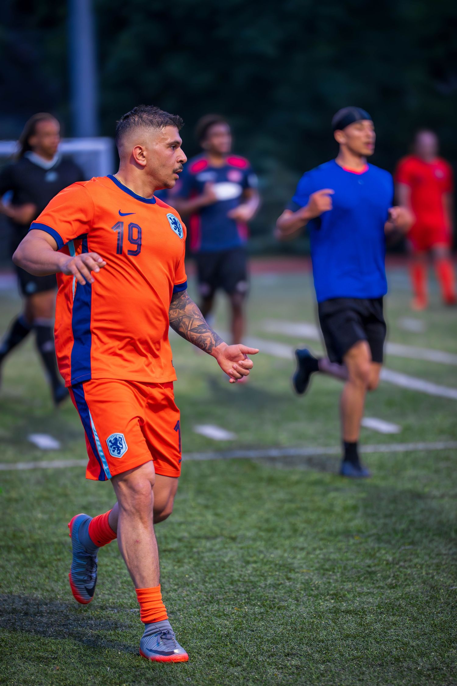 Soccer player in orange jersey gestures while running during evening match.