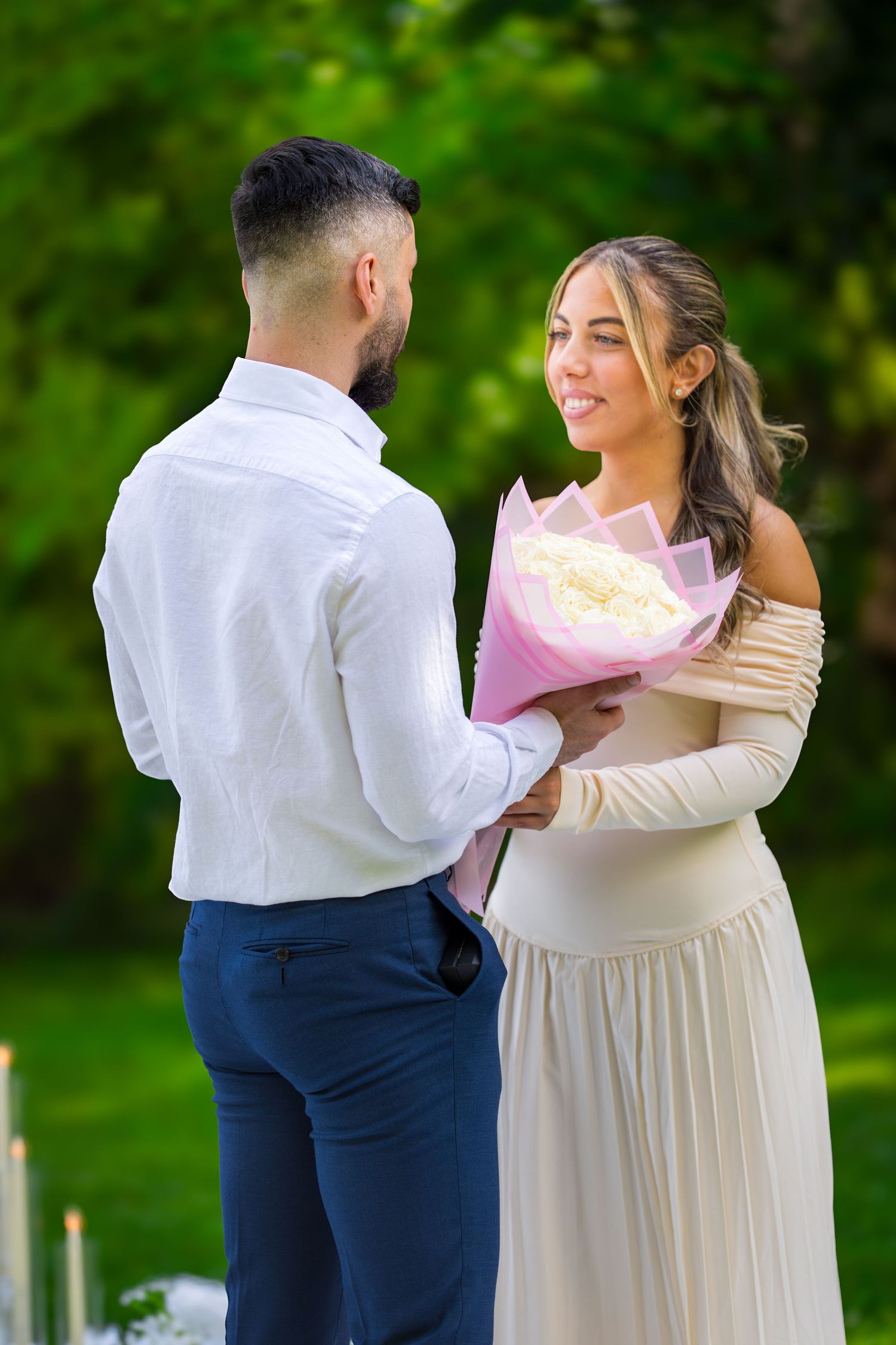 A couple shares a tender moment during a surprise gift reveal in an outdoor garden setting.