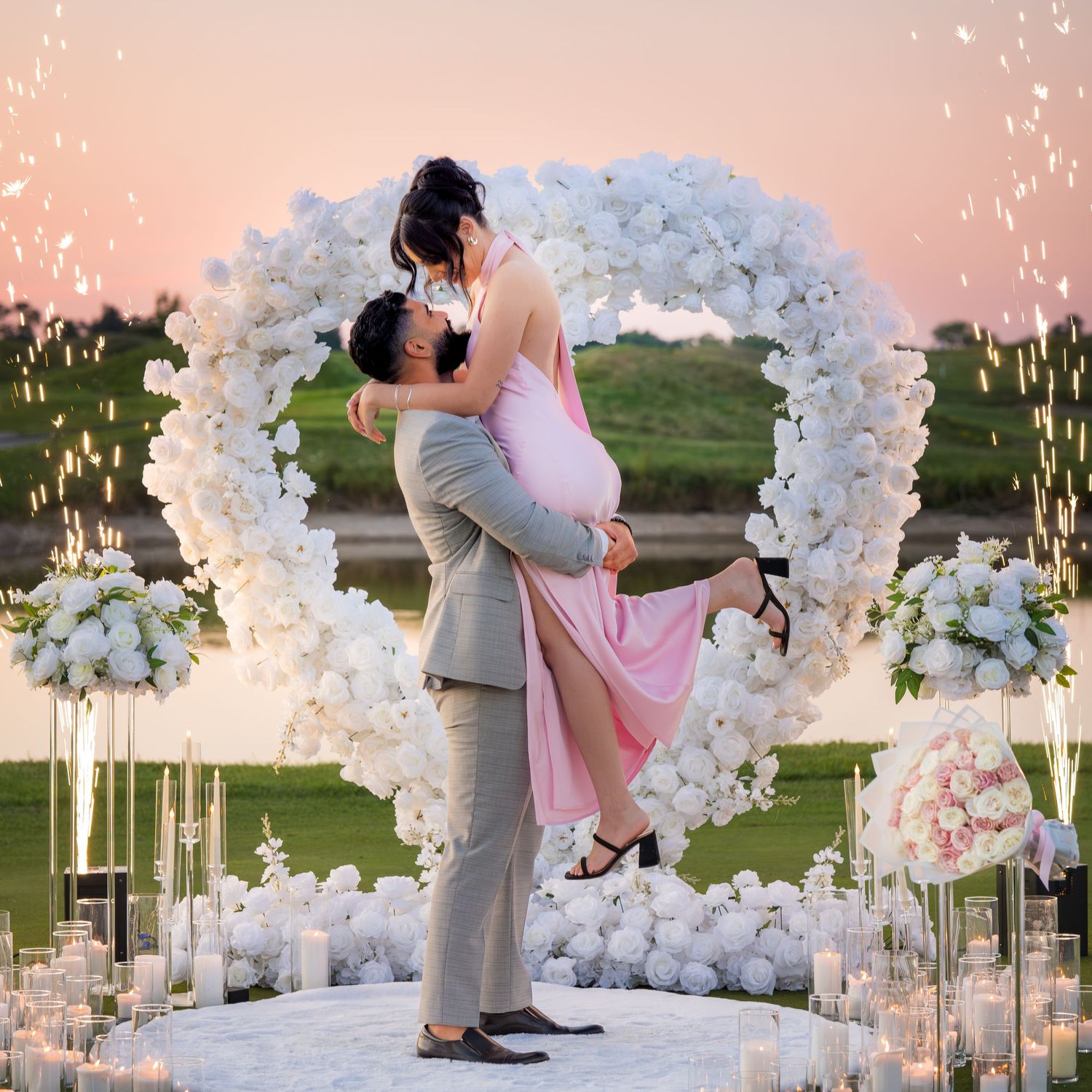 Romantic couple embraces near white floral arch during outdoor sunset photoshoot.
