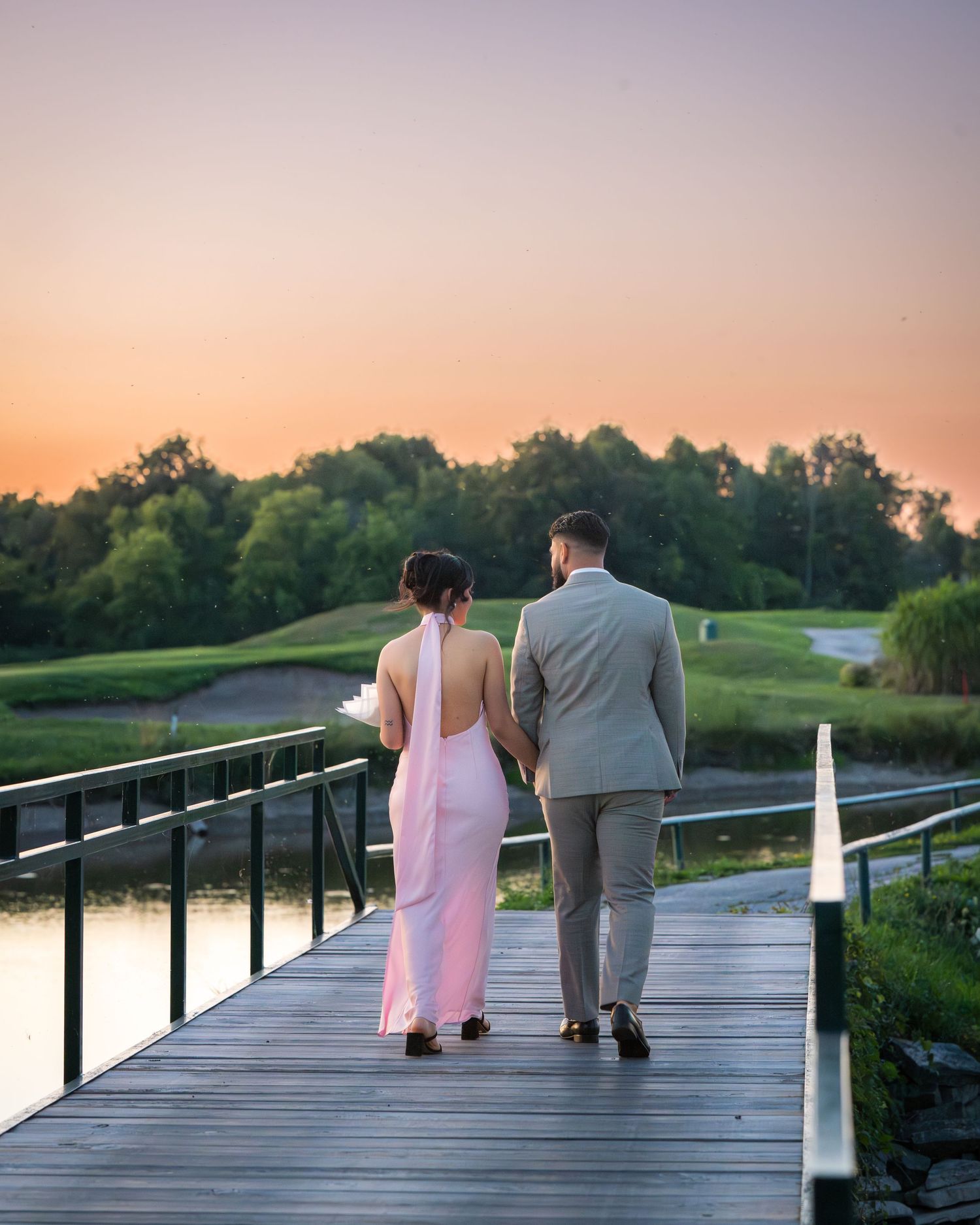 A couple sits together on a wooden boardwalk during sunset with a lake view.