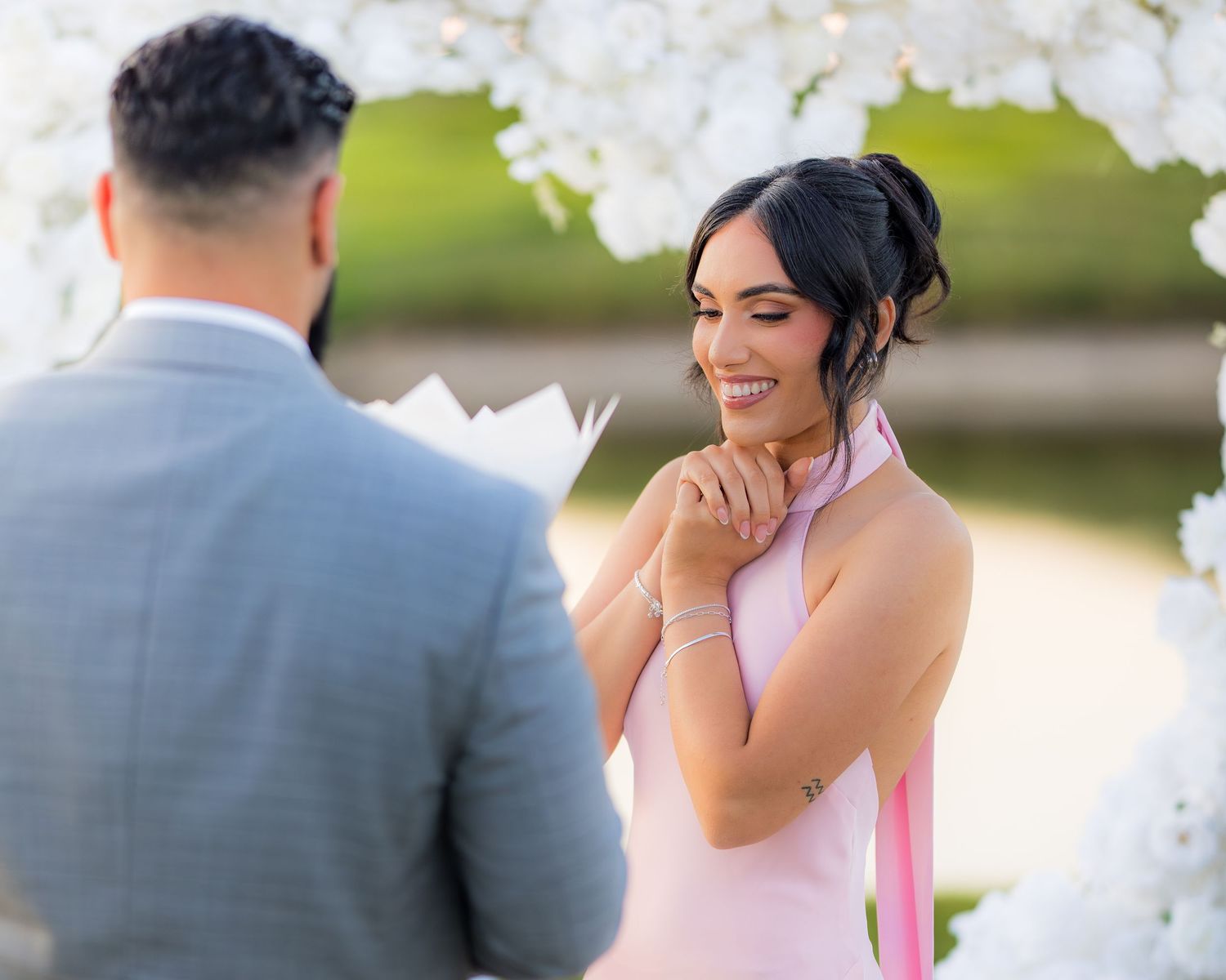 Emotional reaction during surprise proposal under floral arch at sunset.